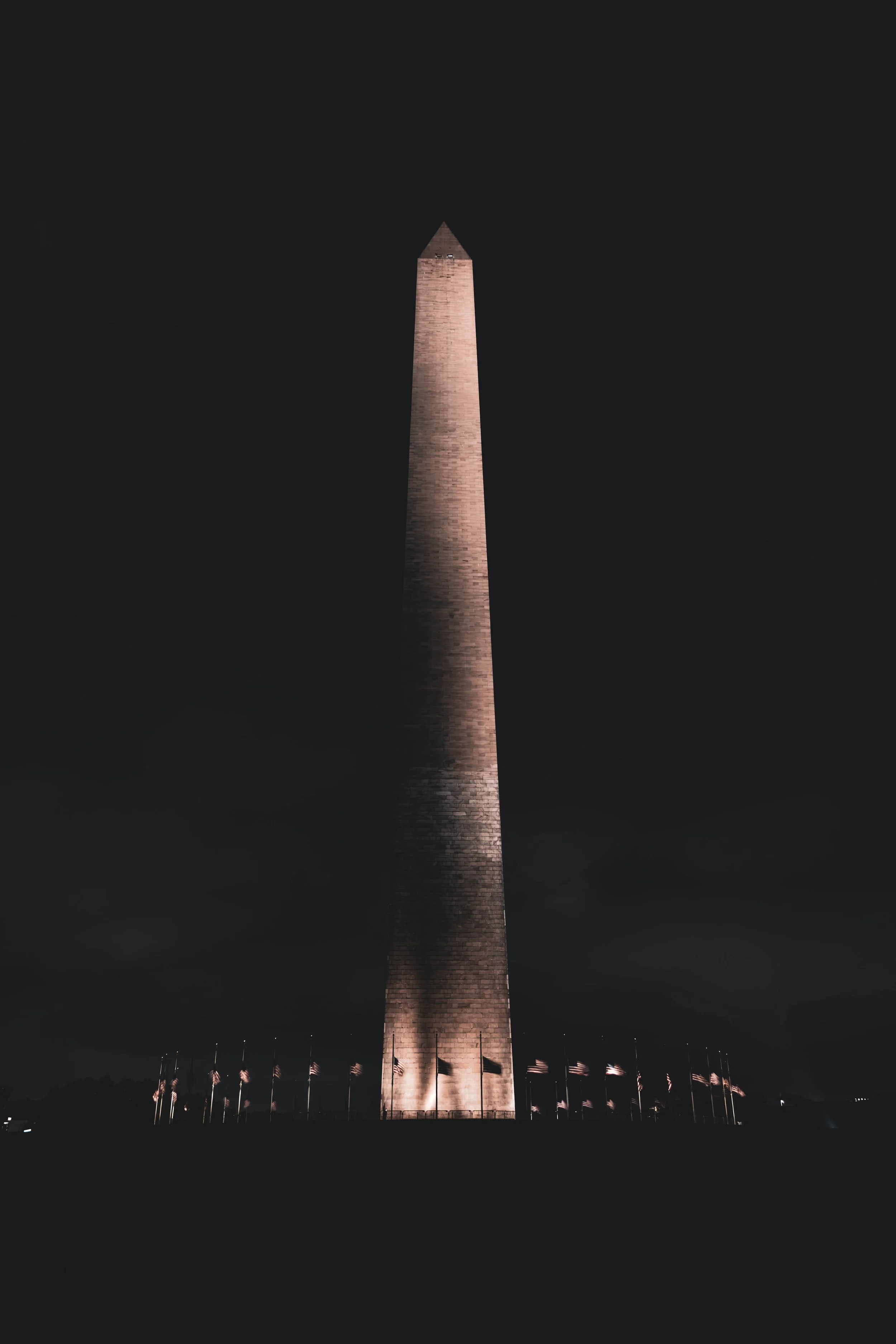 Nighttime view of the Washington Monument illuminated, with American flags surrounding its base.