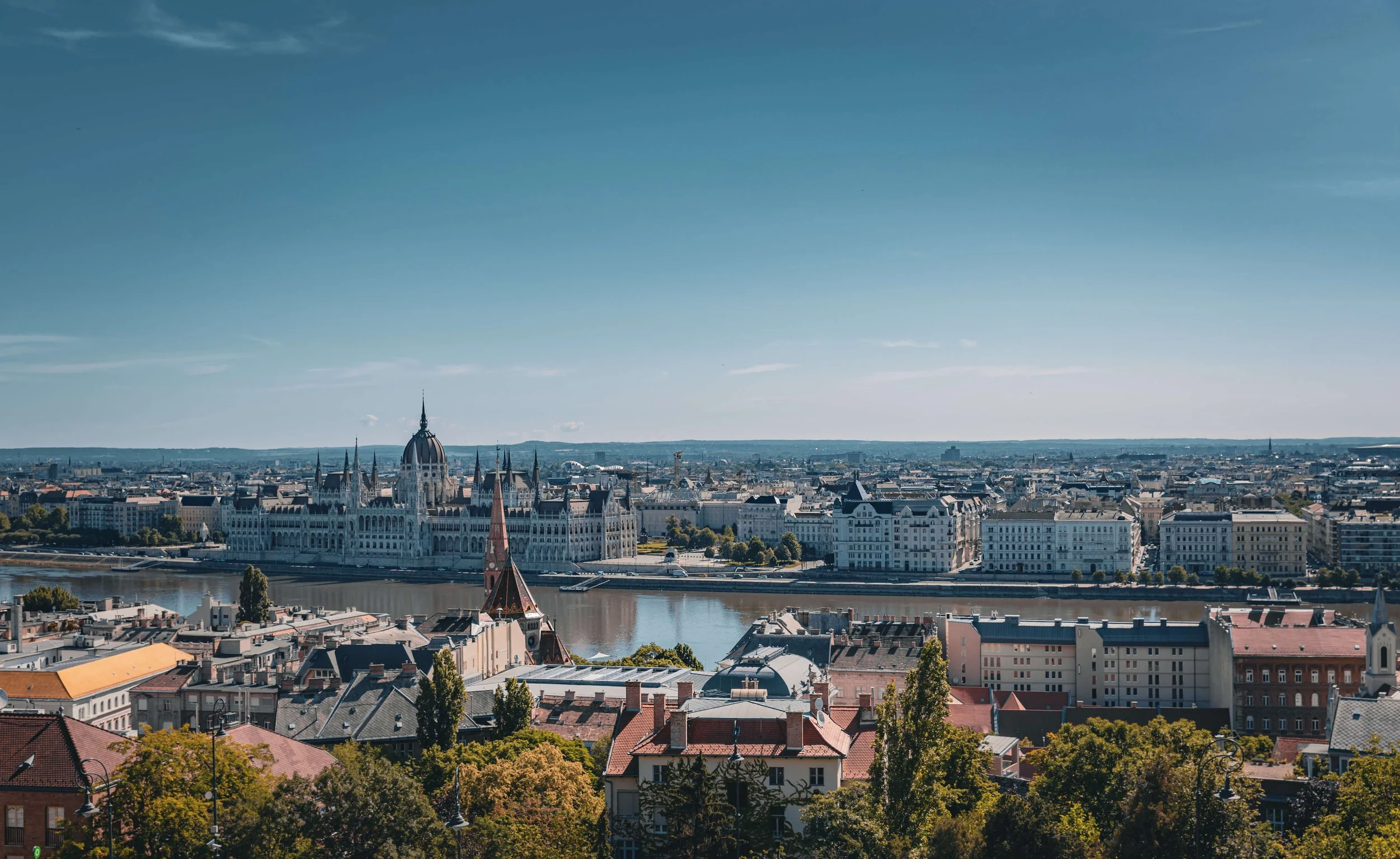 Cityscape of Budapest with Parliament Building and Danube River under a clear blue sky.