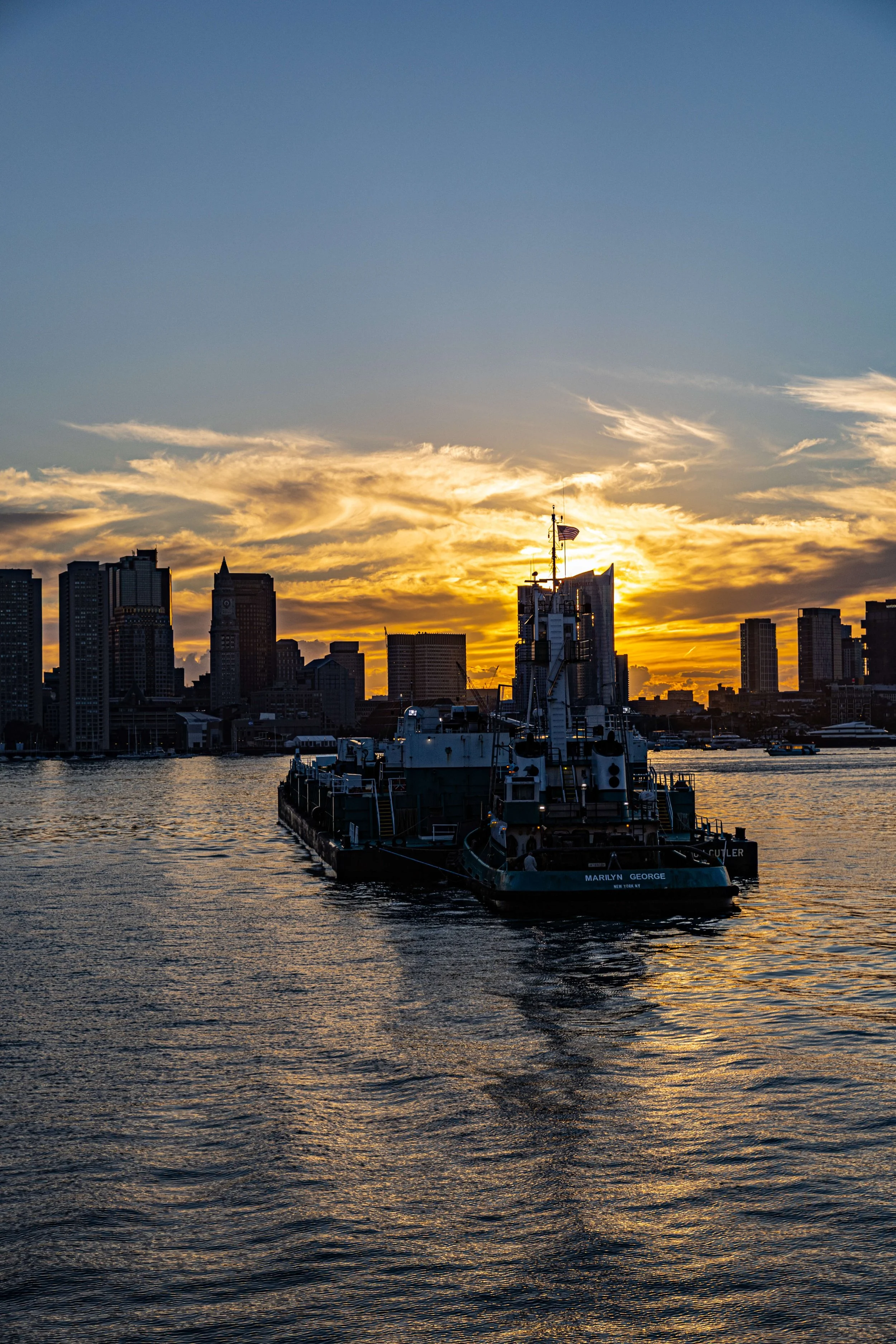 A boat on water with a city skyline at sunset in the background.