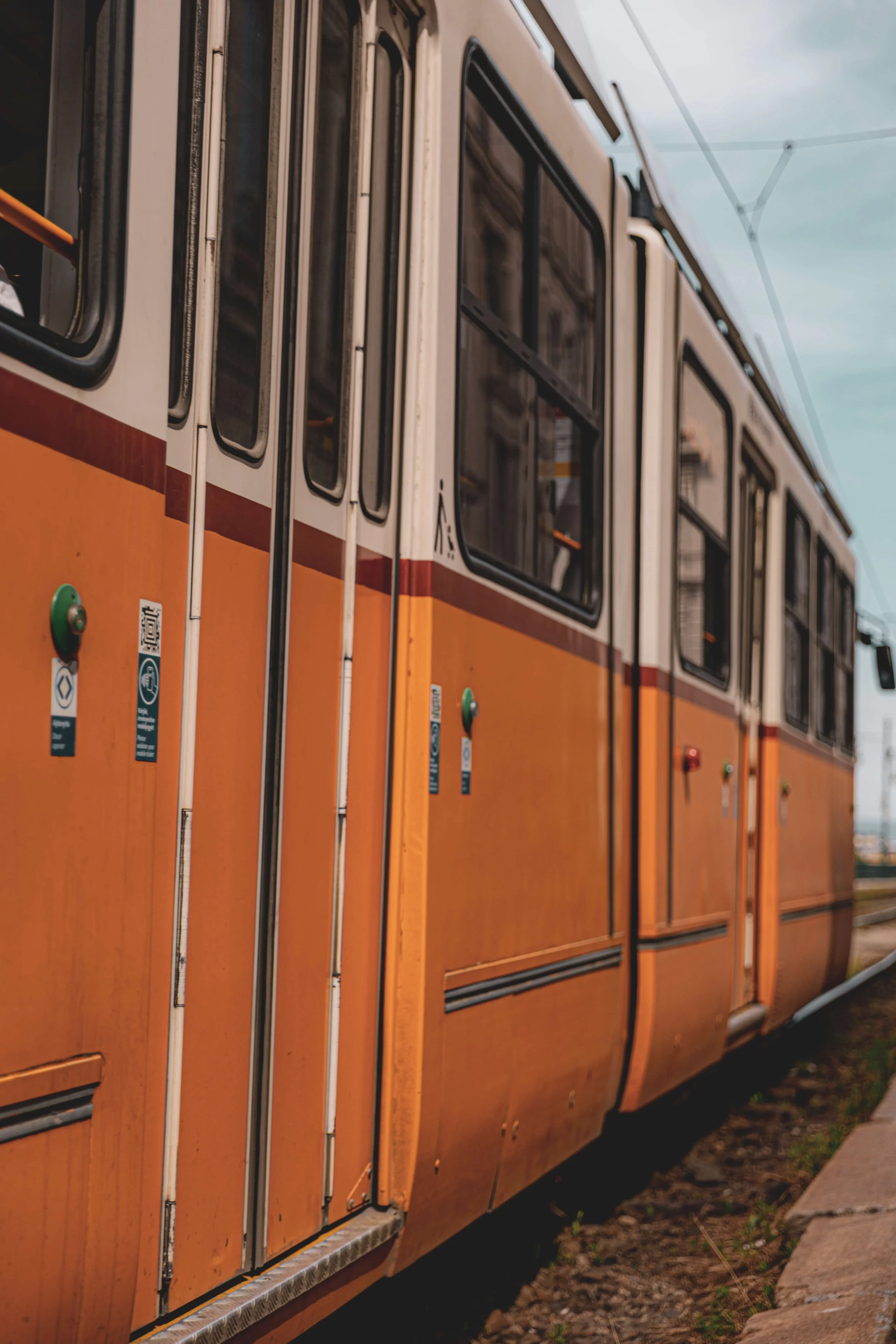Close-up of an orange streetcar with black window frames, parked on a street, with a cloudy sky overhead.