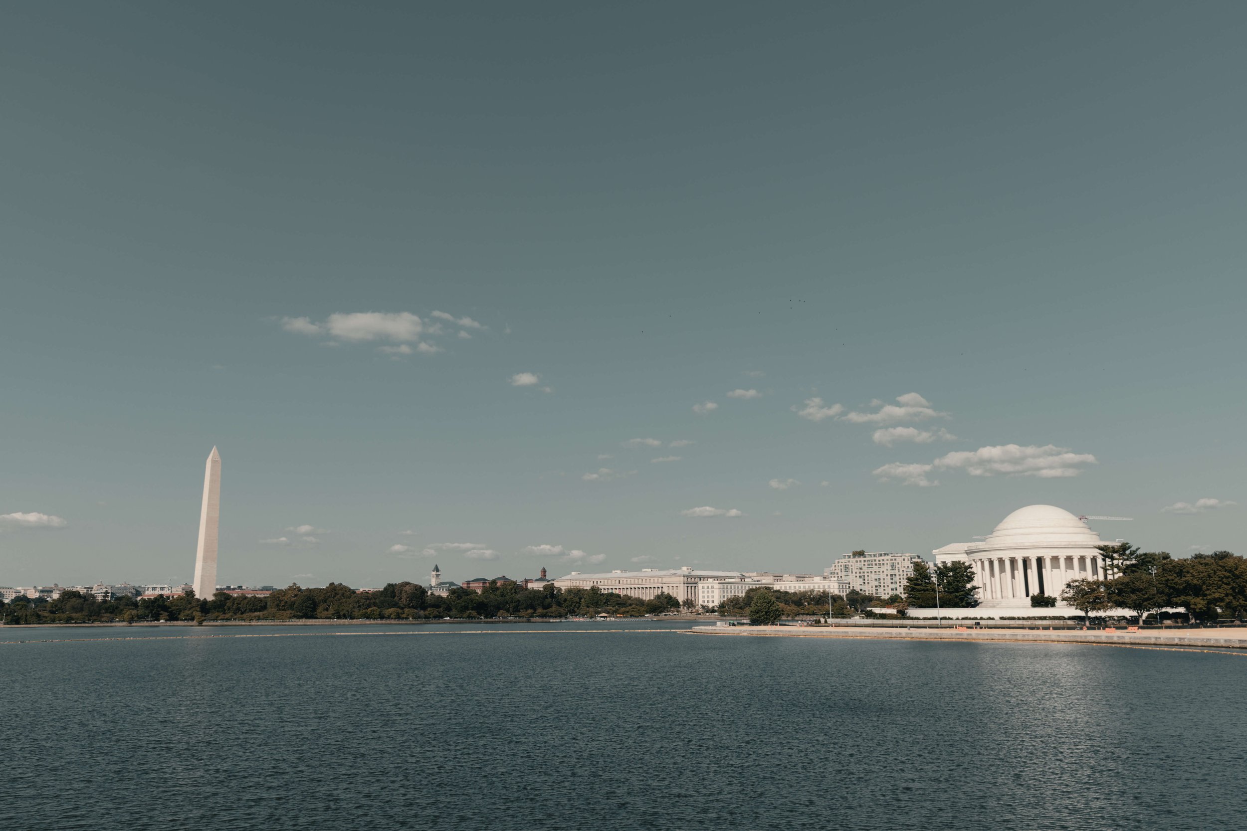 View of the Washington, D.C. skyline with the Washington Monument on the left and the Jefferson Memorial on the right, across a body of water under a partly cloudy sky.