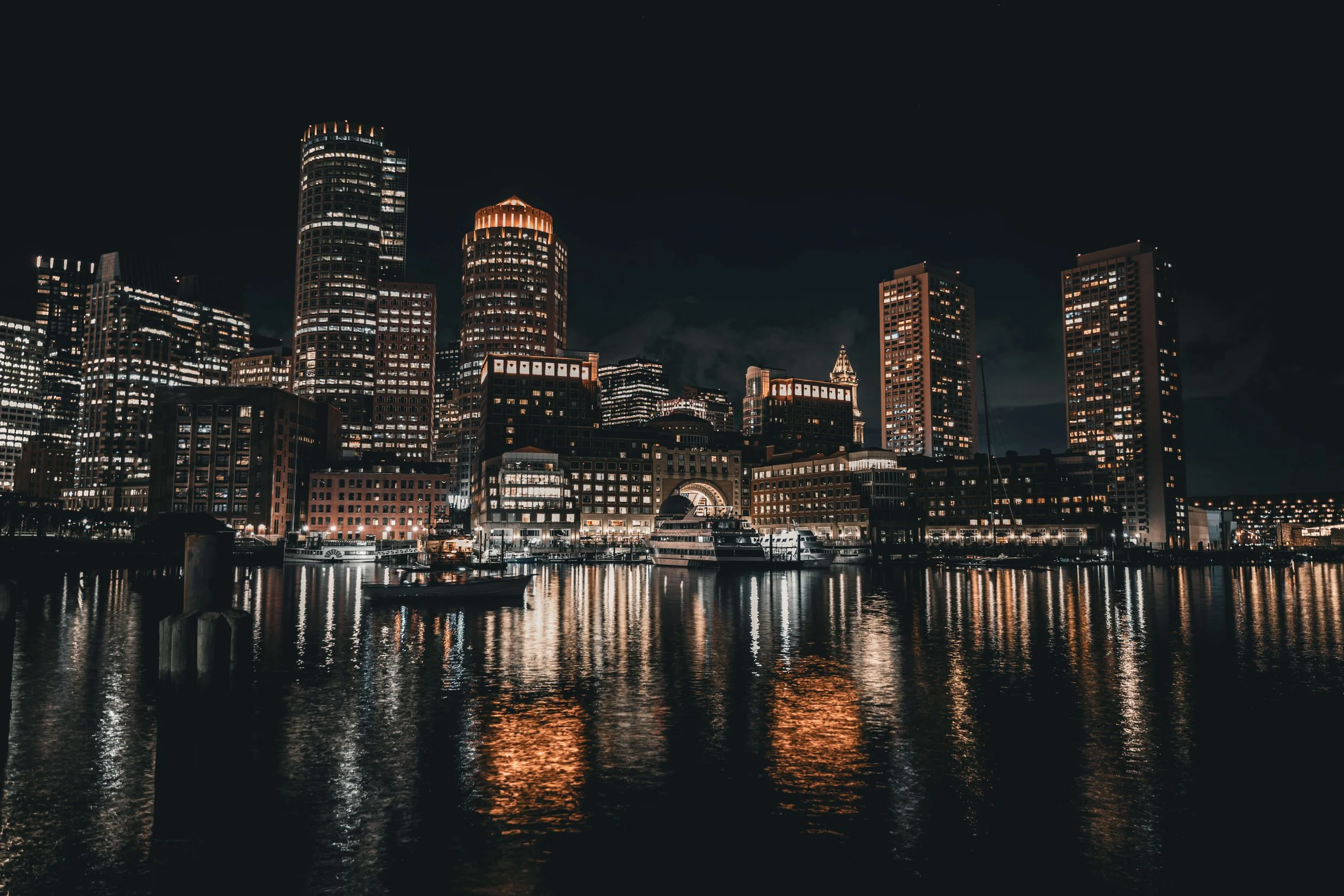 Night view of a city skyline with tall illuminated buildings reflected in the water.