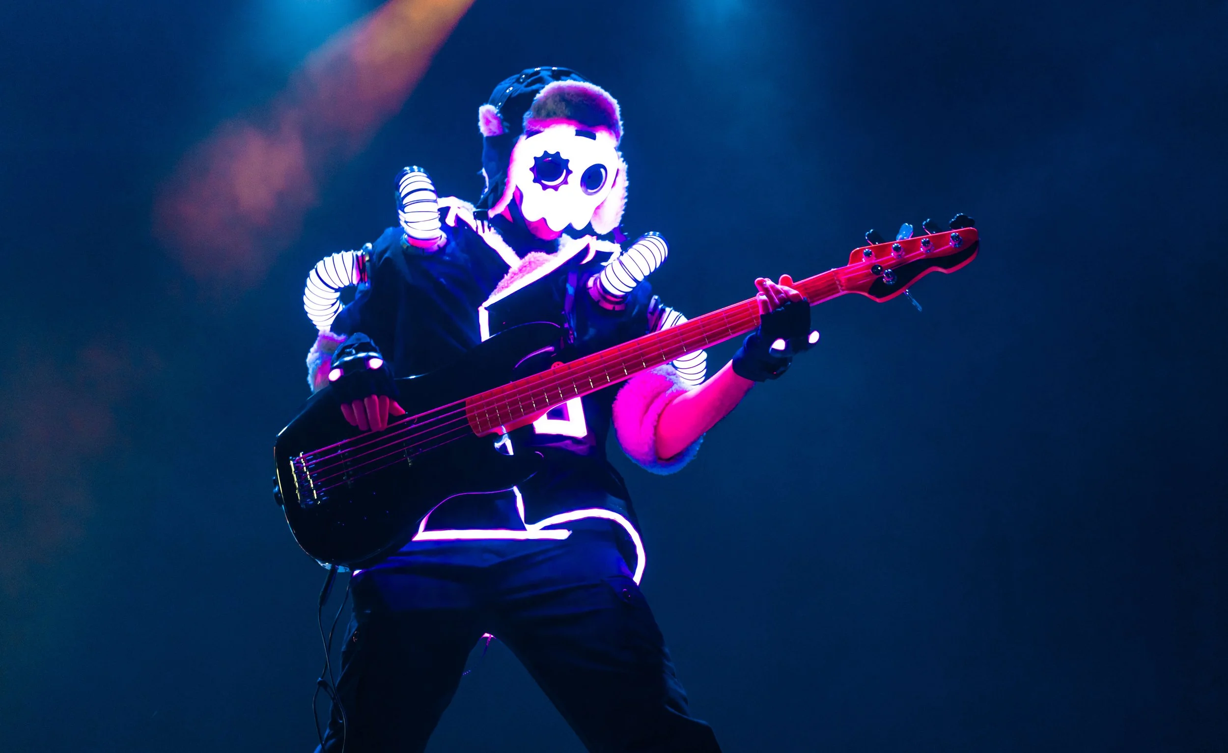 A person wearing a mascot mask playing an electric guitar on stage with colorful lights.