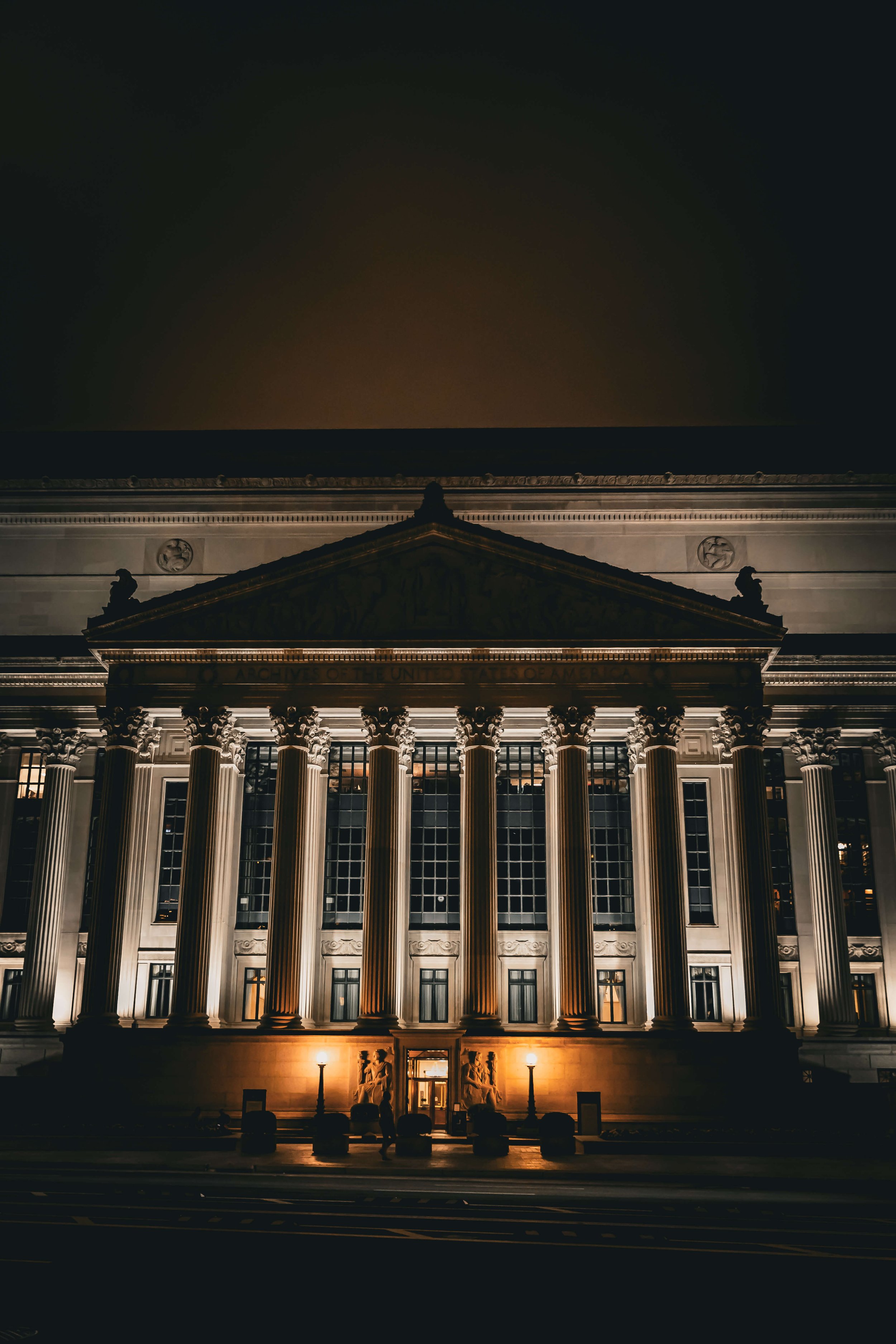 Night view of a grand, historic building with tall columns illuminated from below, with a dark sky in the background.