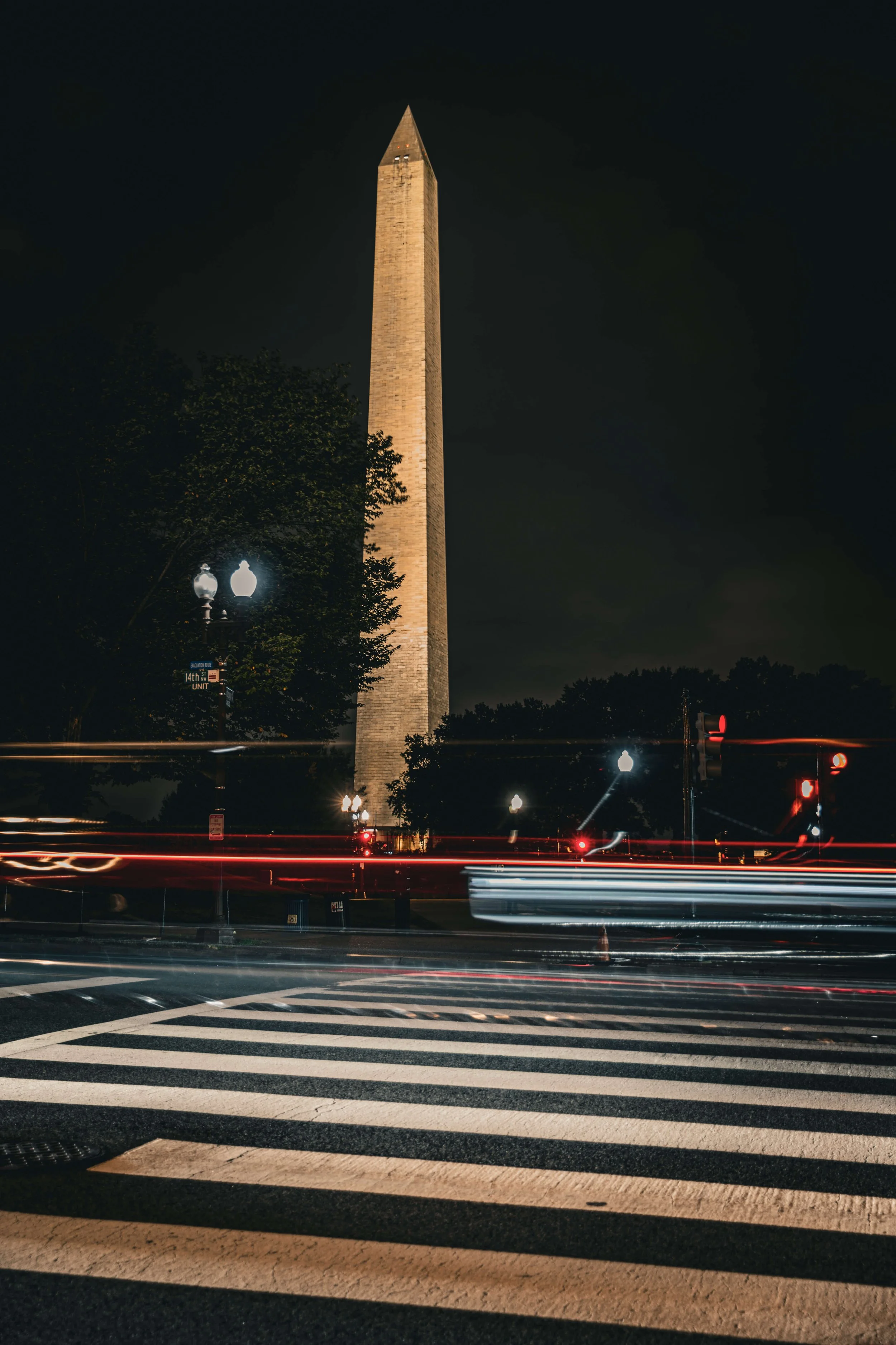 Nighttime photo of the Washington Monument in Washington, D.C., with light trails from passing cars and streetlights in the foreground.