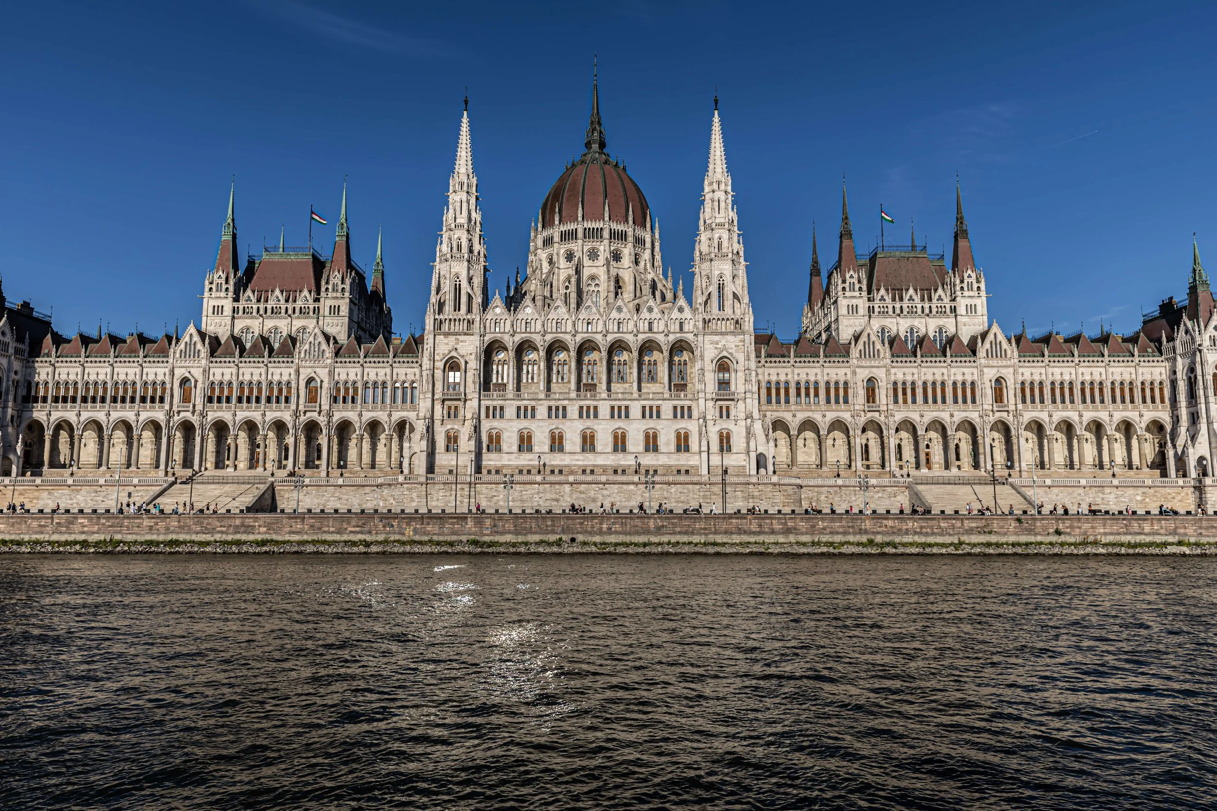 The Parliament building in Budapest, Hungary, viewed from across the Danube River on a clear day with a blue sky.