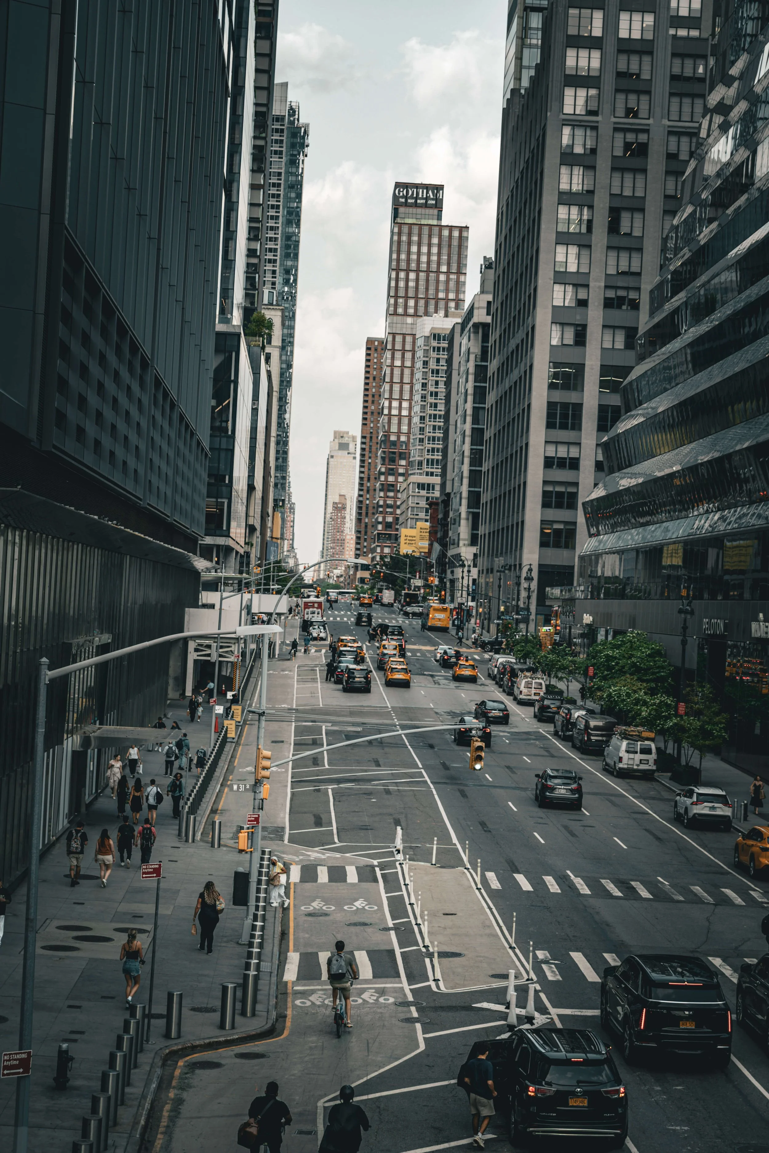 Street view of a busy urban city with tall skyscrapers, cars, taxis, buses, bicycles, and pedestrians on the sidewalks.