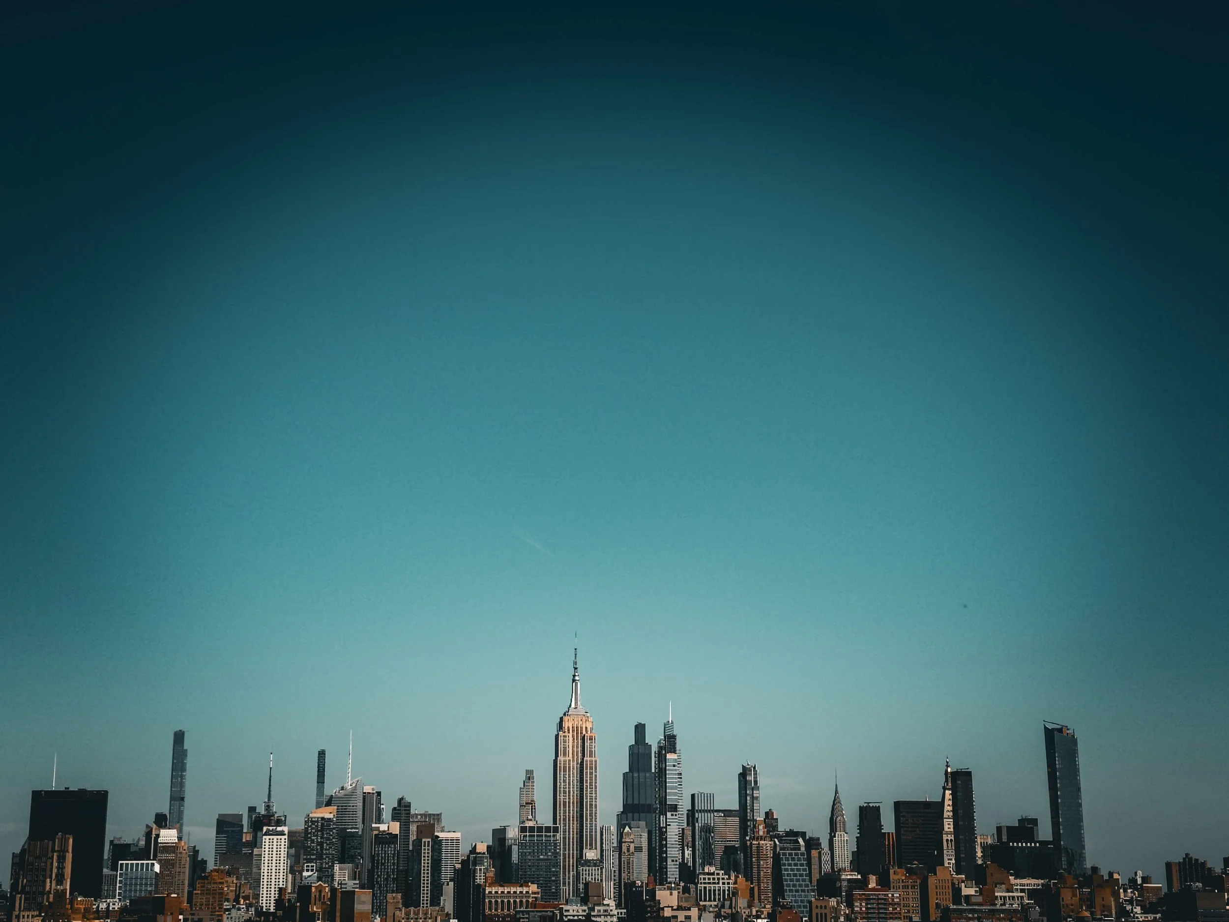 Skyline of New York City with iconic skyscrapers, including the Empire State Building, under a clear blue sky.