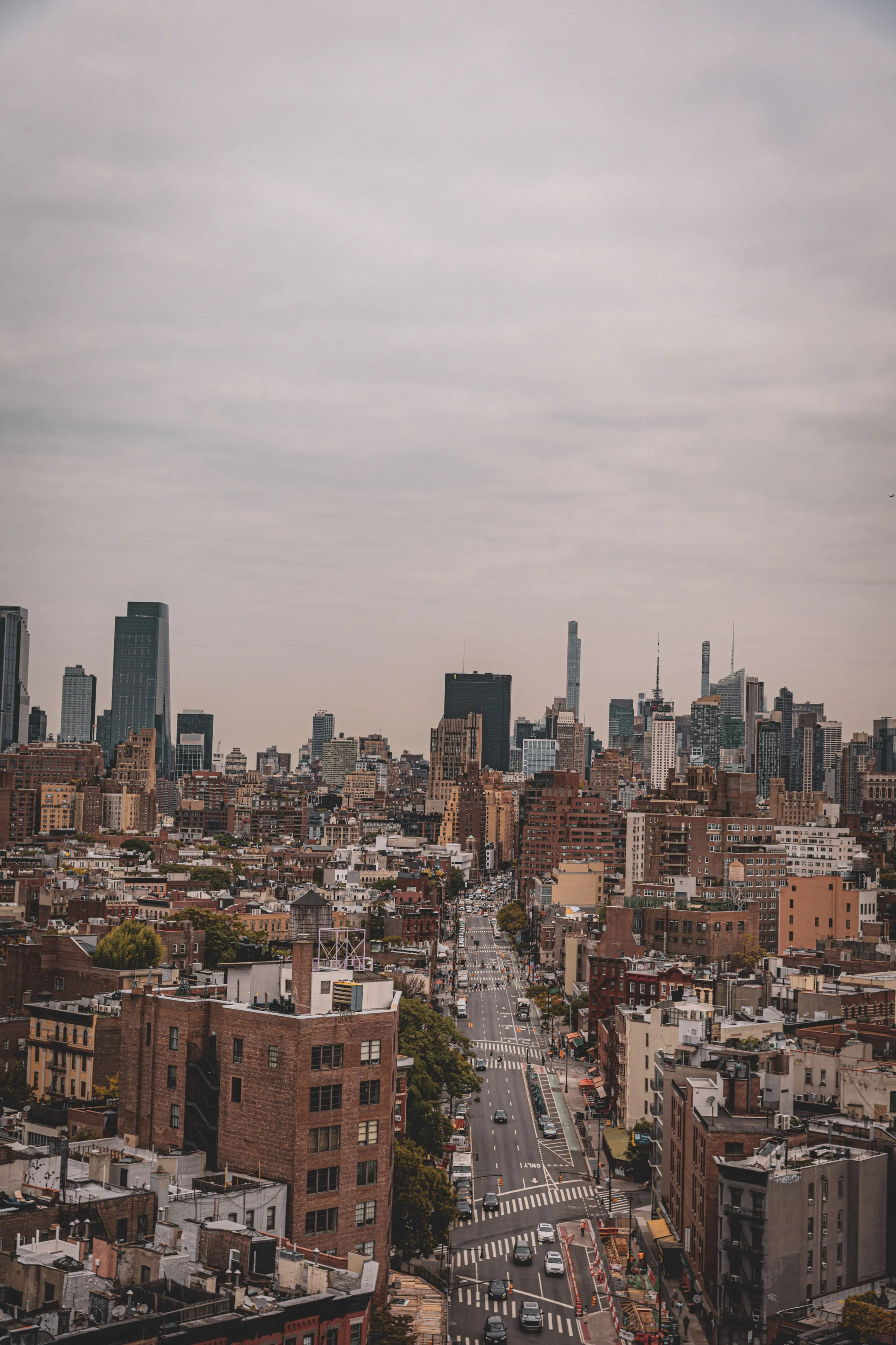 City skyline of Manhattan, New York City, featuring tall skyscrapers, busy streets with cars, crosswalks, and buildings under a cloudy sky.