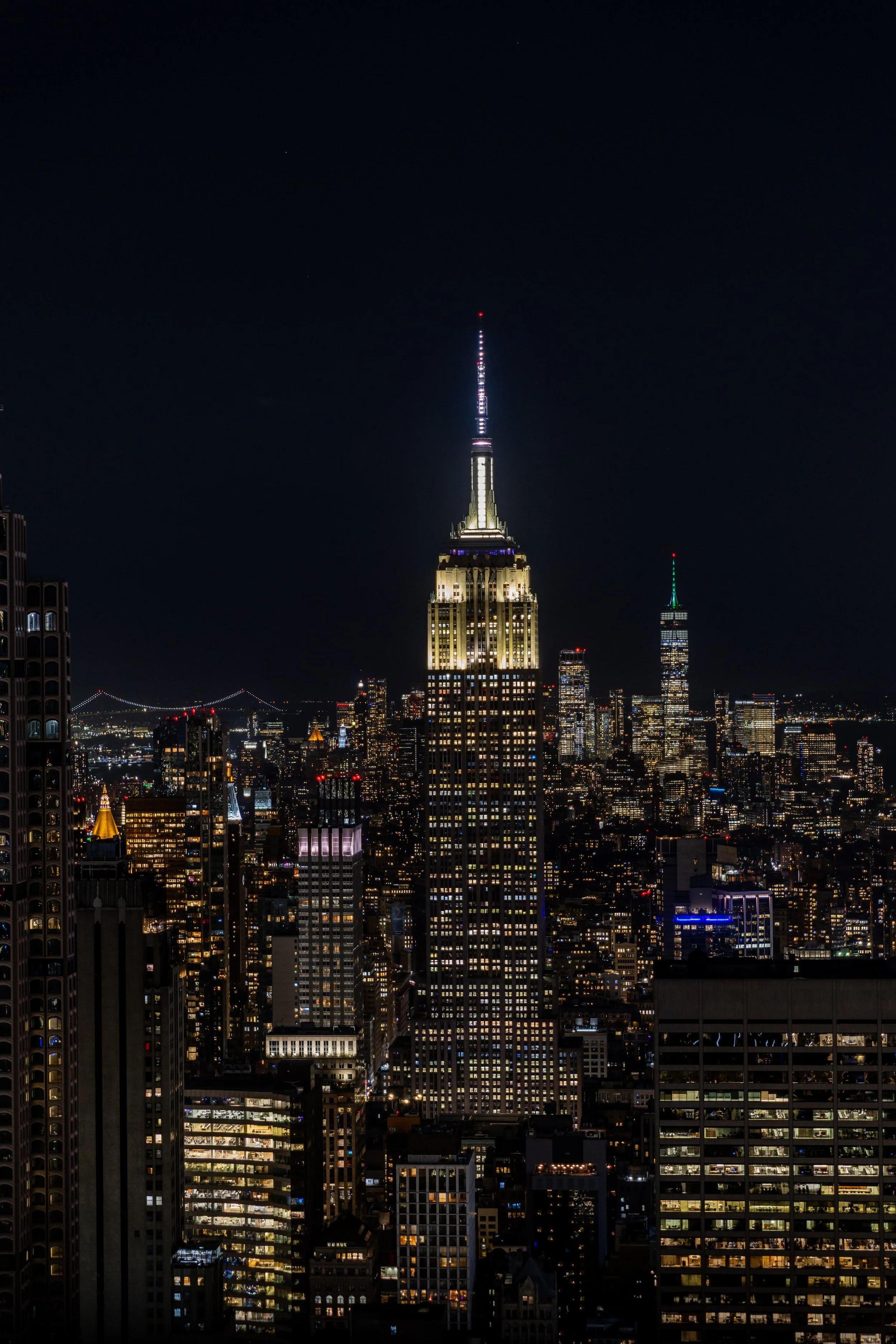 Nighttime view of the New York City skyline featuring the Empire State Building illuminated, with other skyscrapers and city lights in the background.