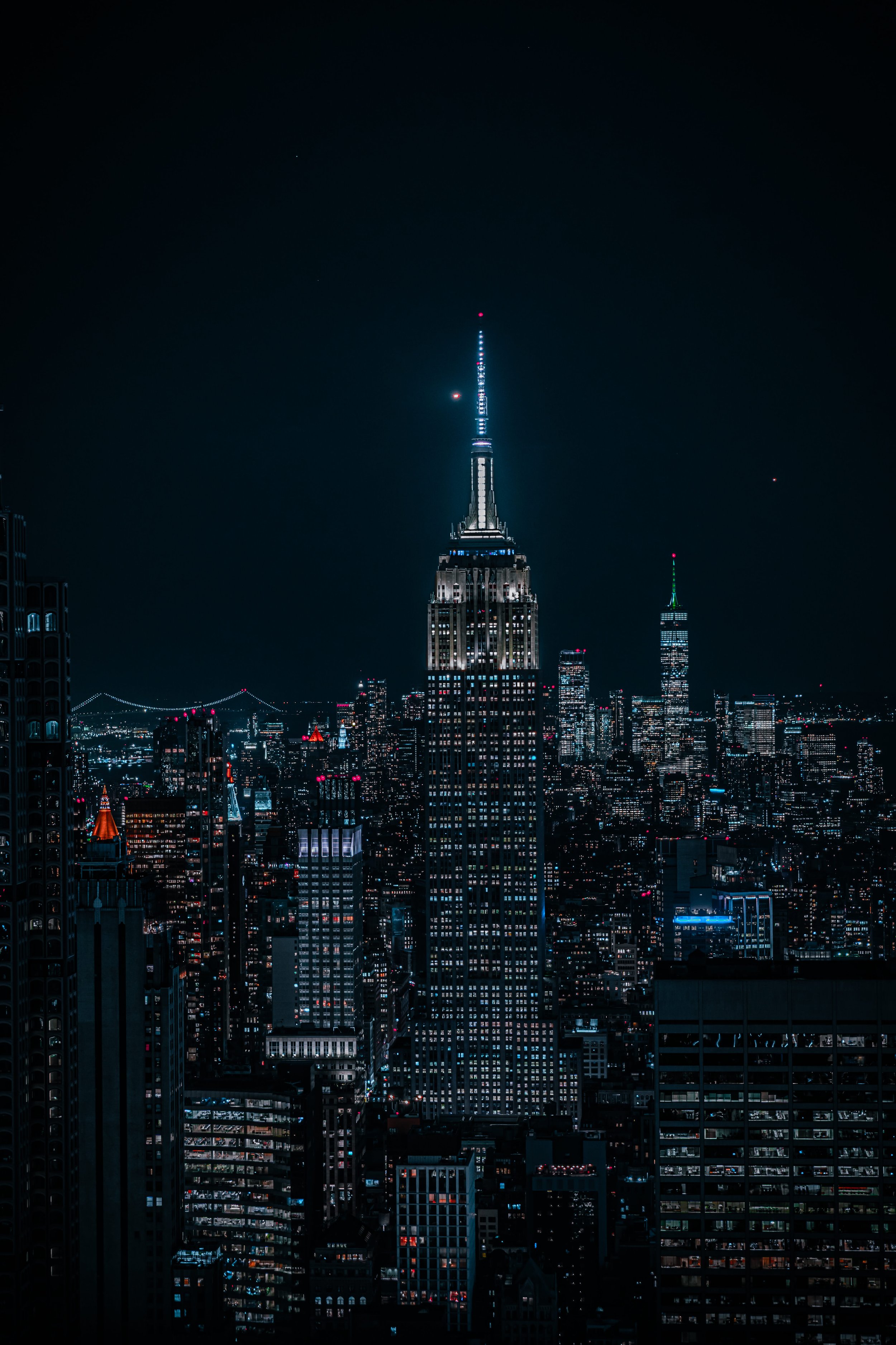 Nighttime aerial view of New York City featuring the Empire State Building illuminated and surrounded by city lights.
