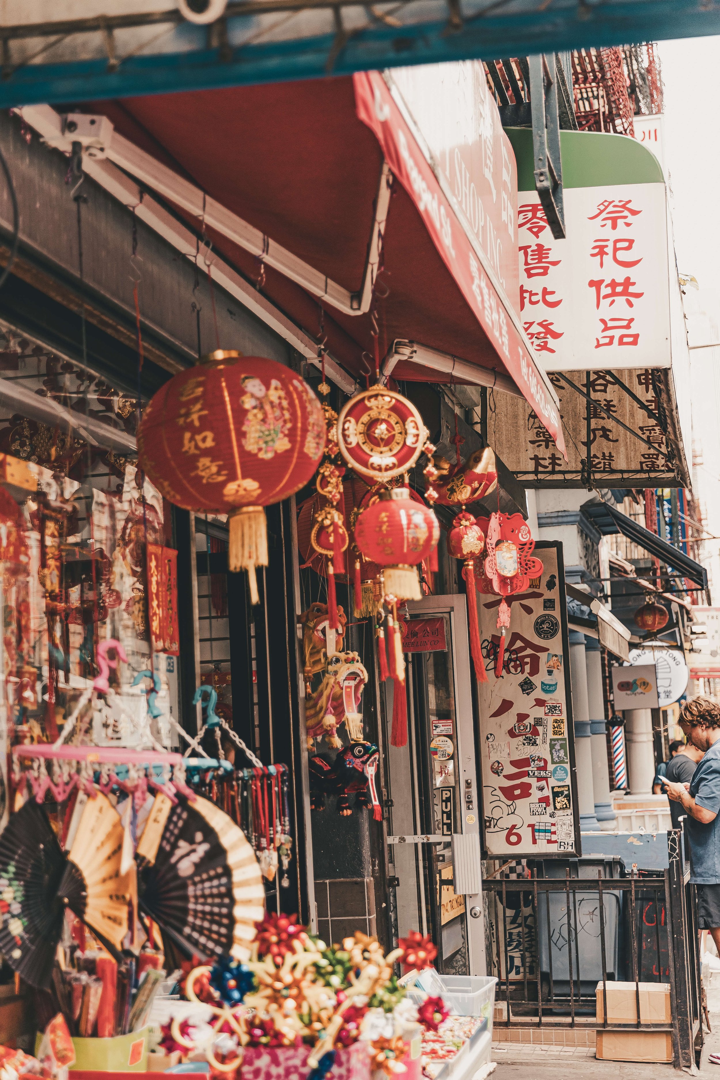 Street scene of a shop with red Chinese lanterns and decorations, and a man standing nearby using his phone.