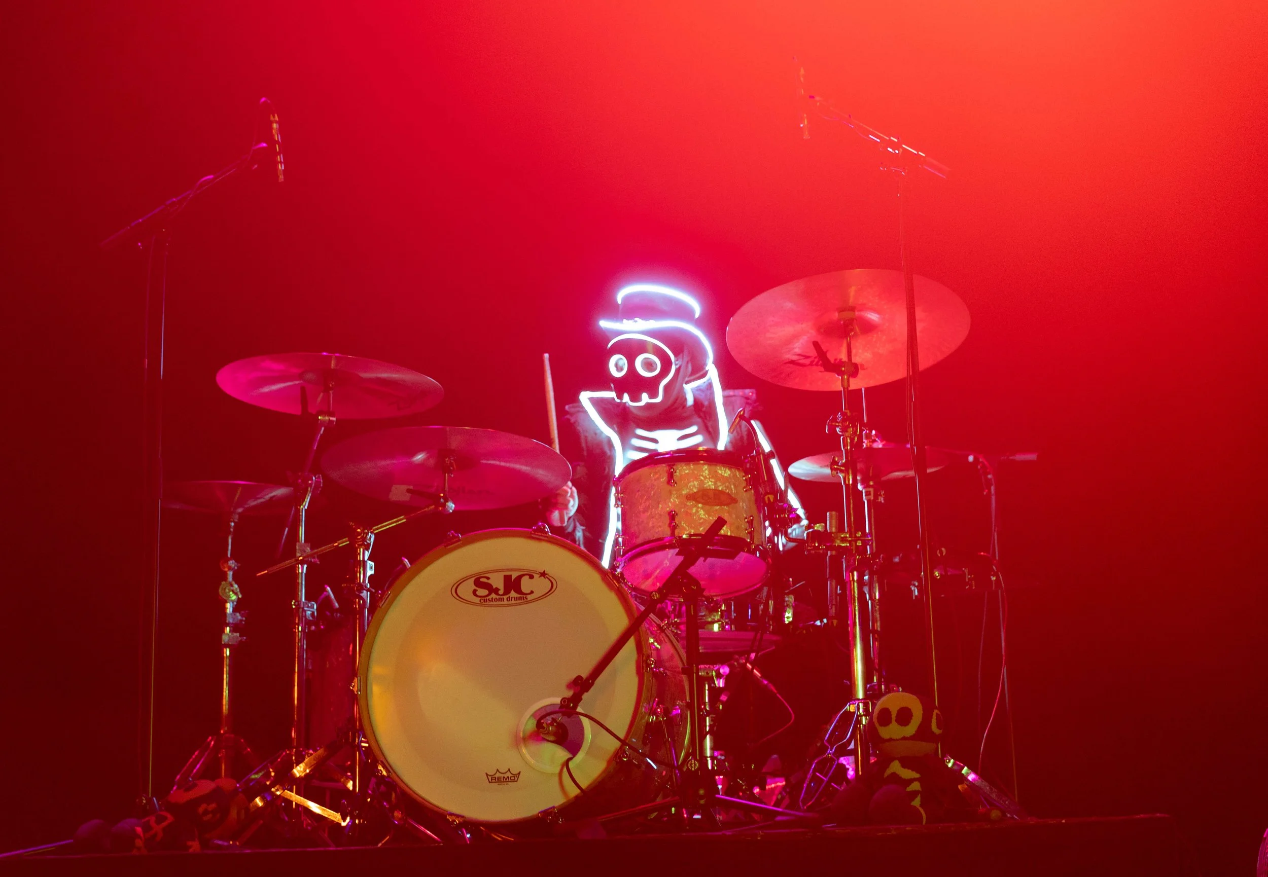 A drums set illuminated with neon signs, including a skull and flame design, on a stage with red lighting.