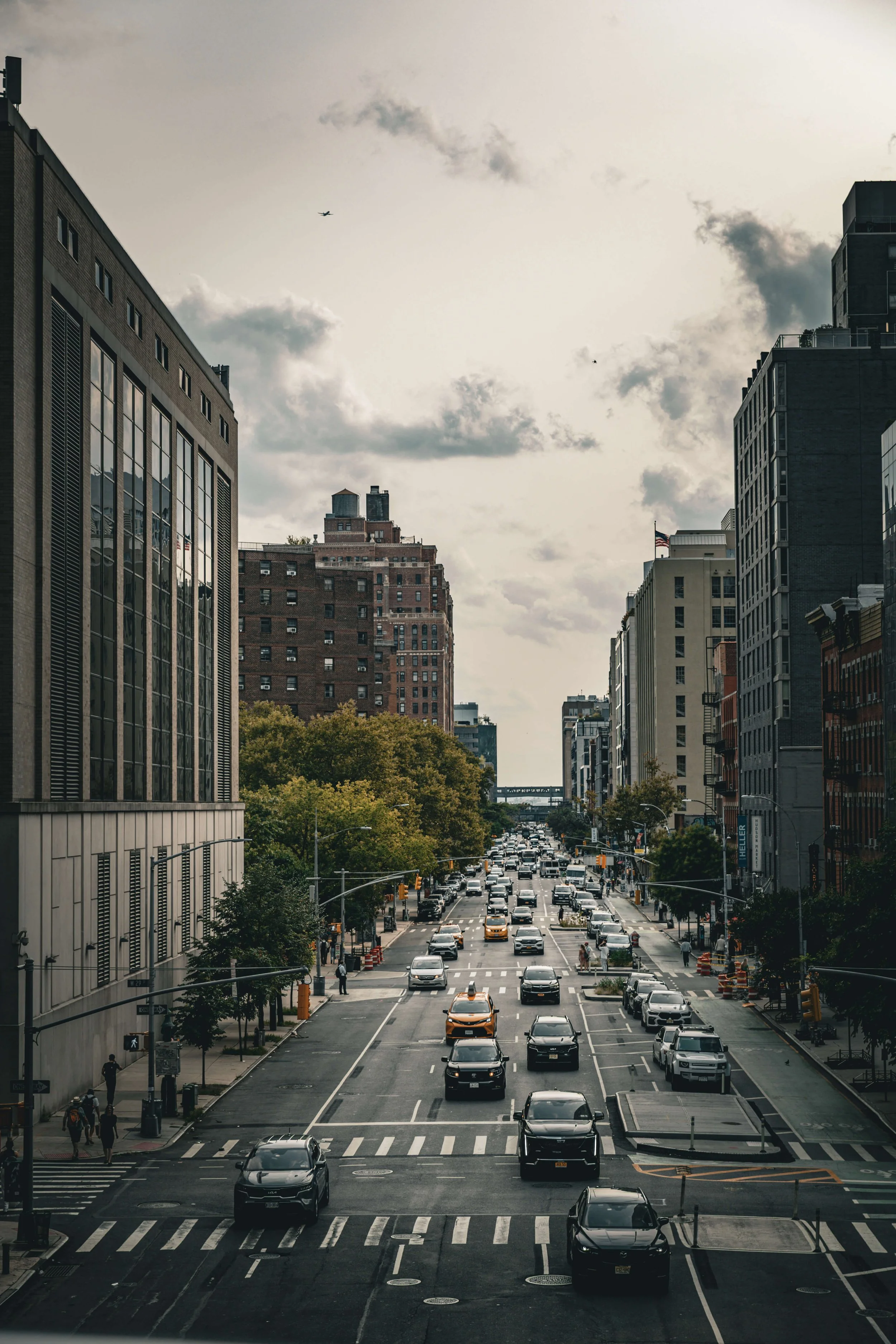 Urban street scene with cars, buildings, trees, and a cloudy sky.