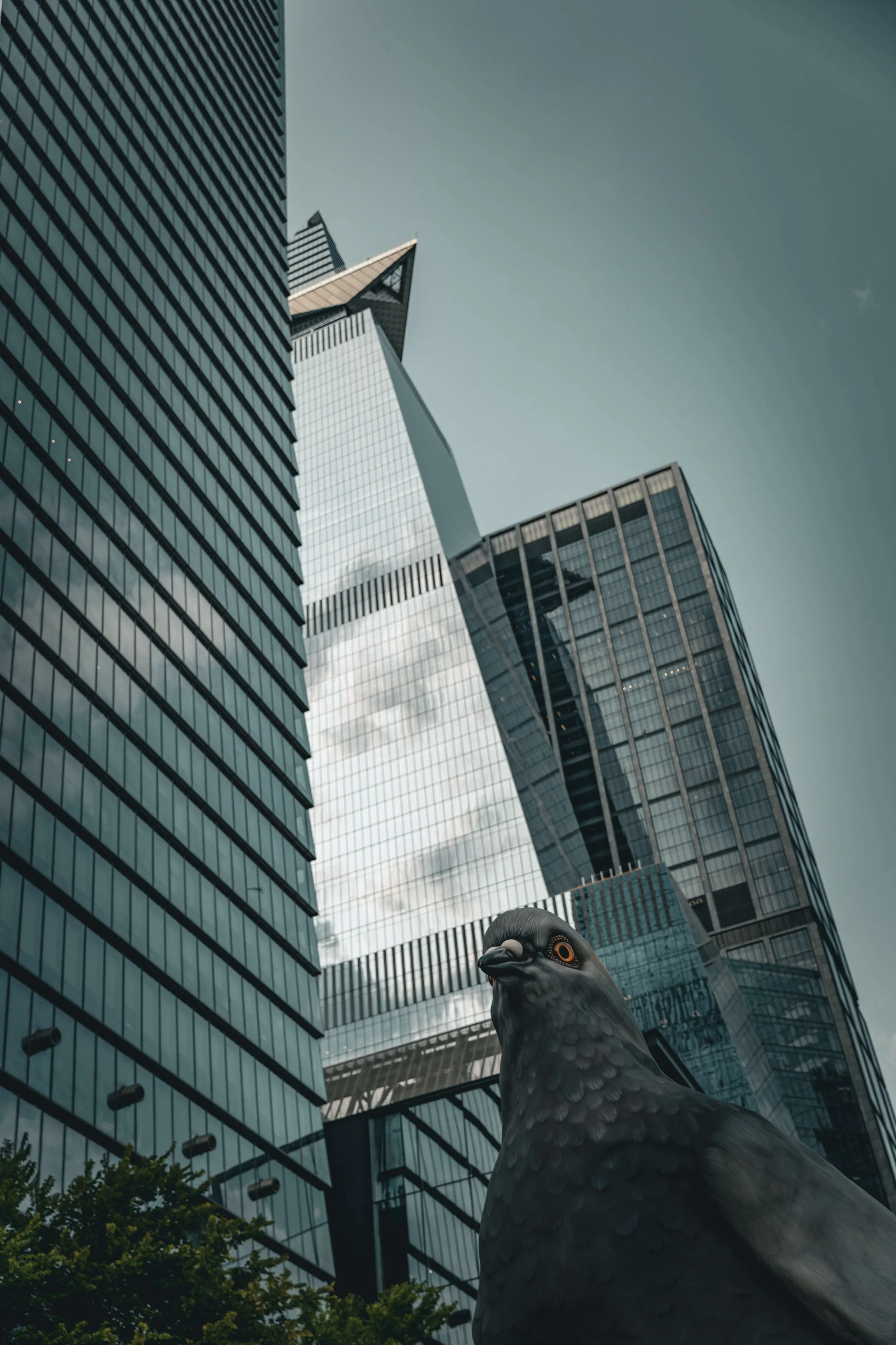 A low-angle view of skyscrapers in a city, with a large pigeon sculpture in the foreground.