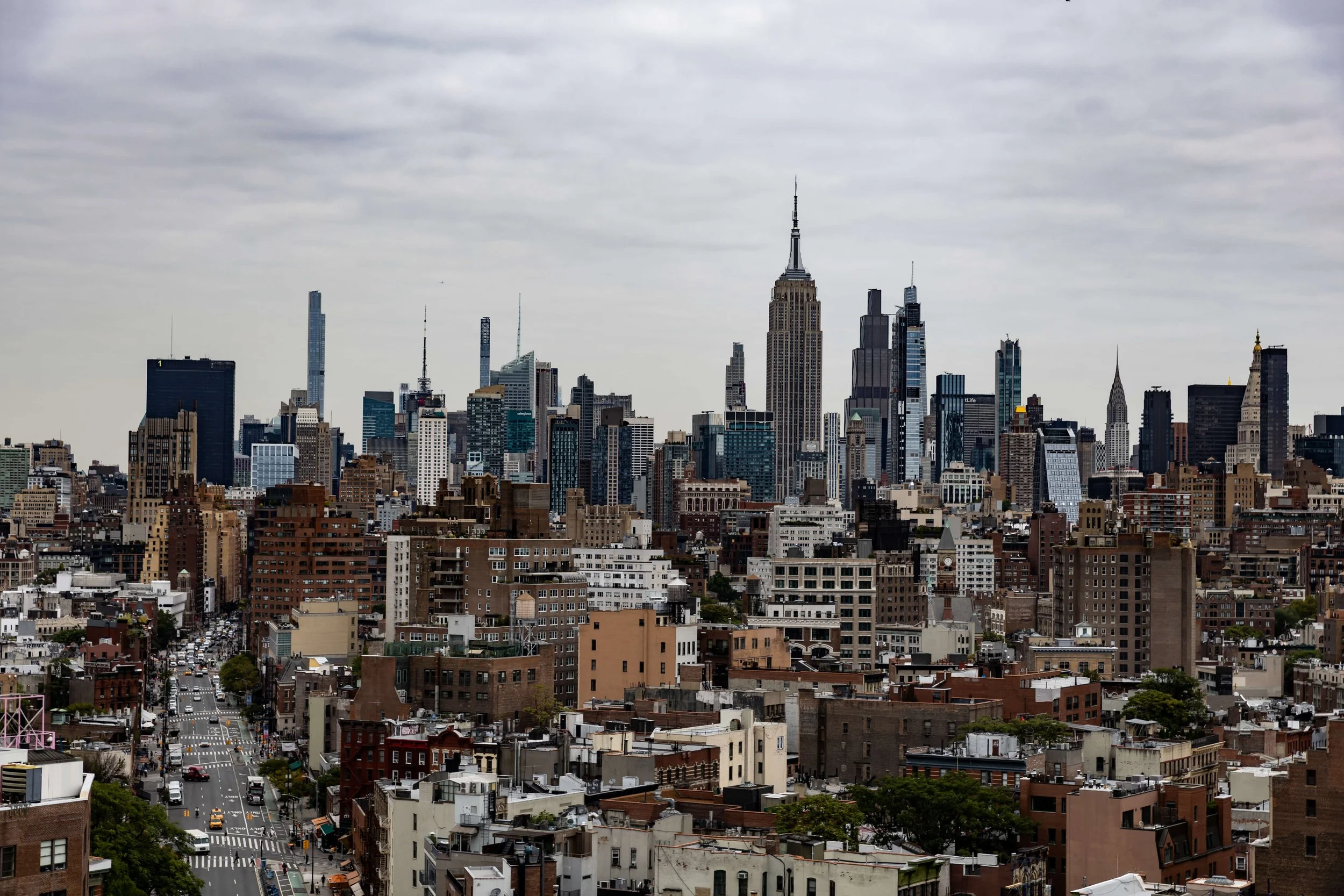 A city skyline featuring tall skyscrapers, including the Empire State Building, on a cloudy day.