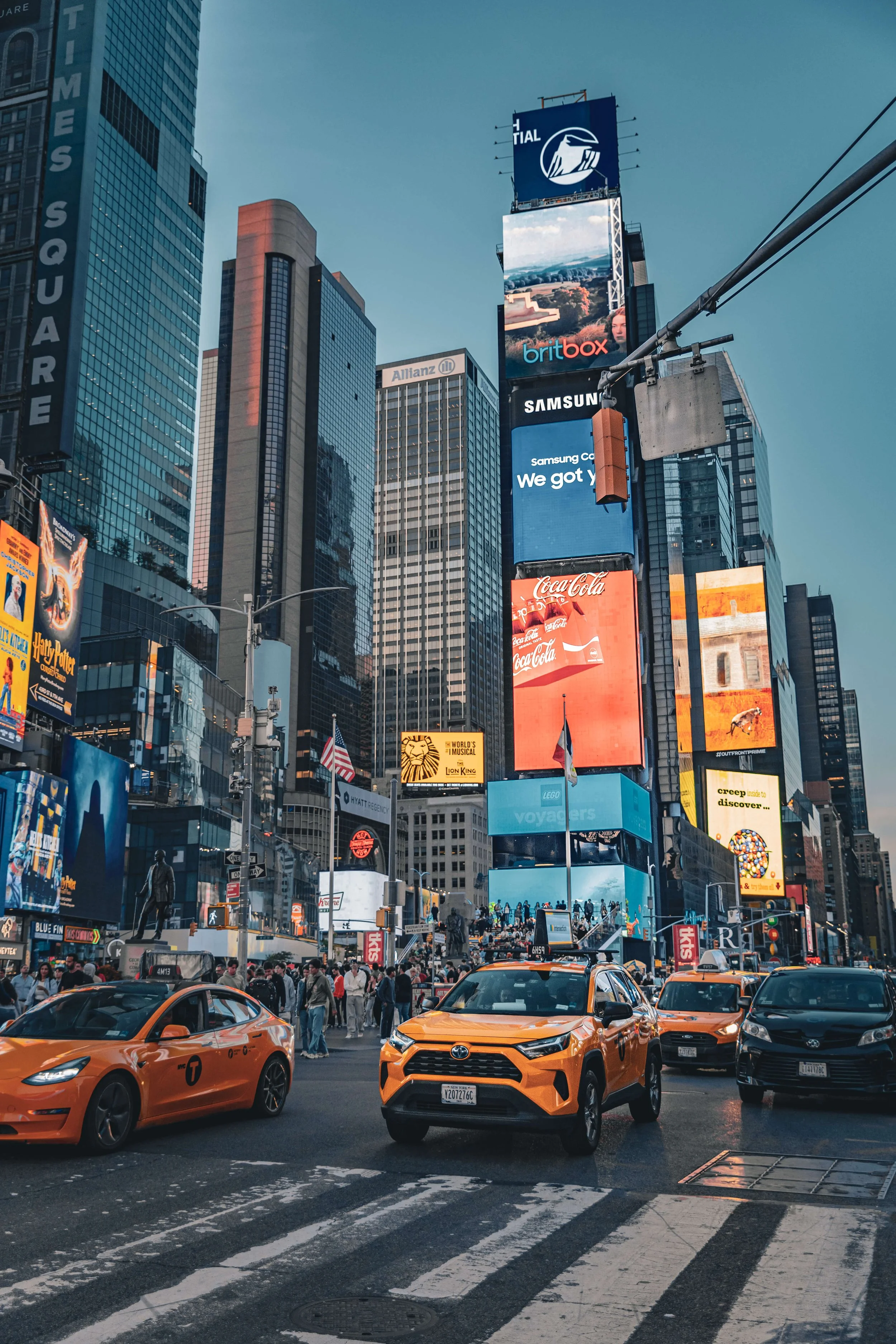 Times Square in New York City with tall buildings, electronic billboards, yellow taxis, and crowds of people.