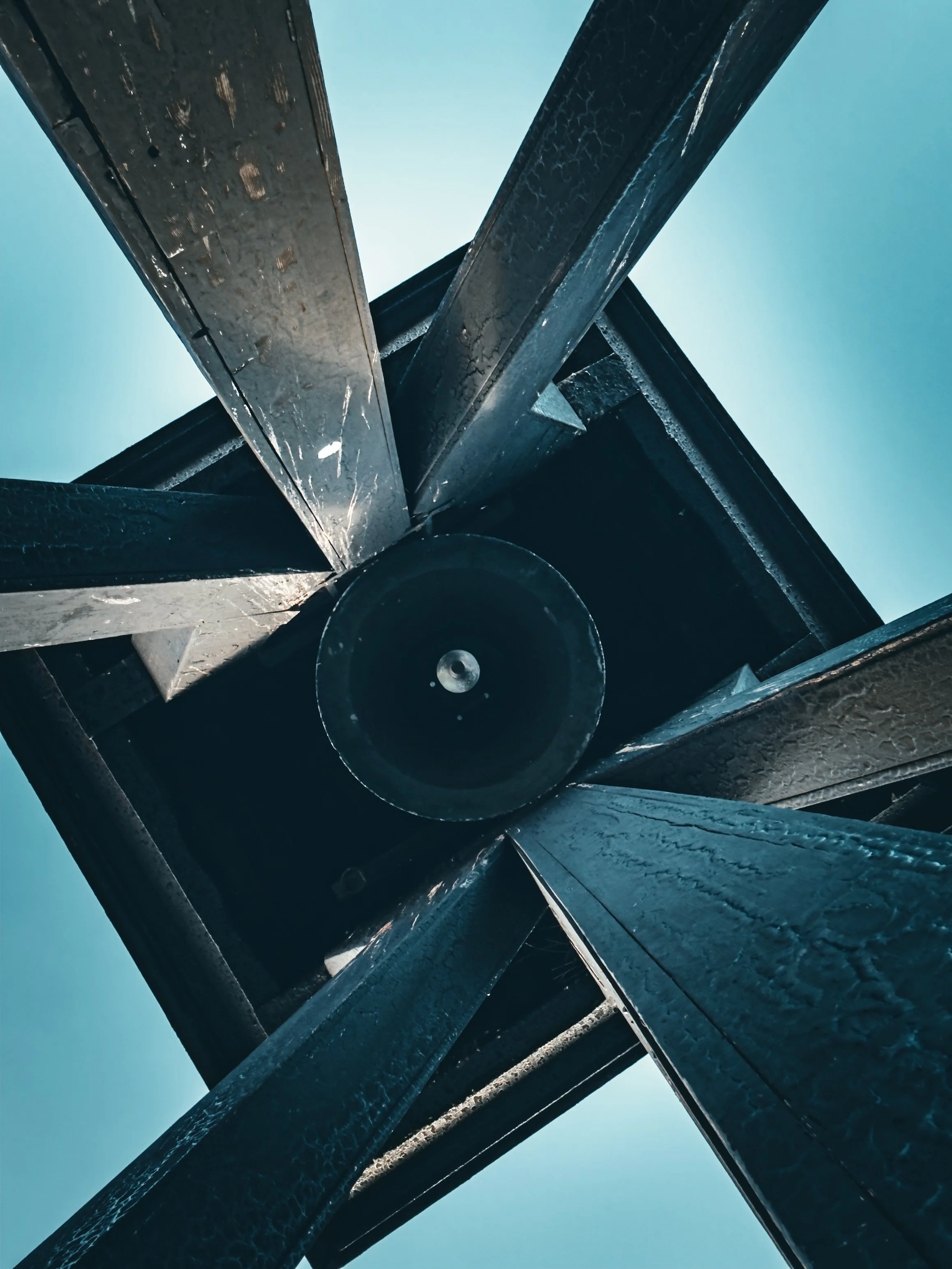 Looking up at a black metal windmill structure against a blue sky.