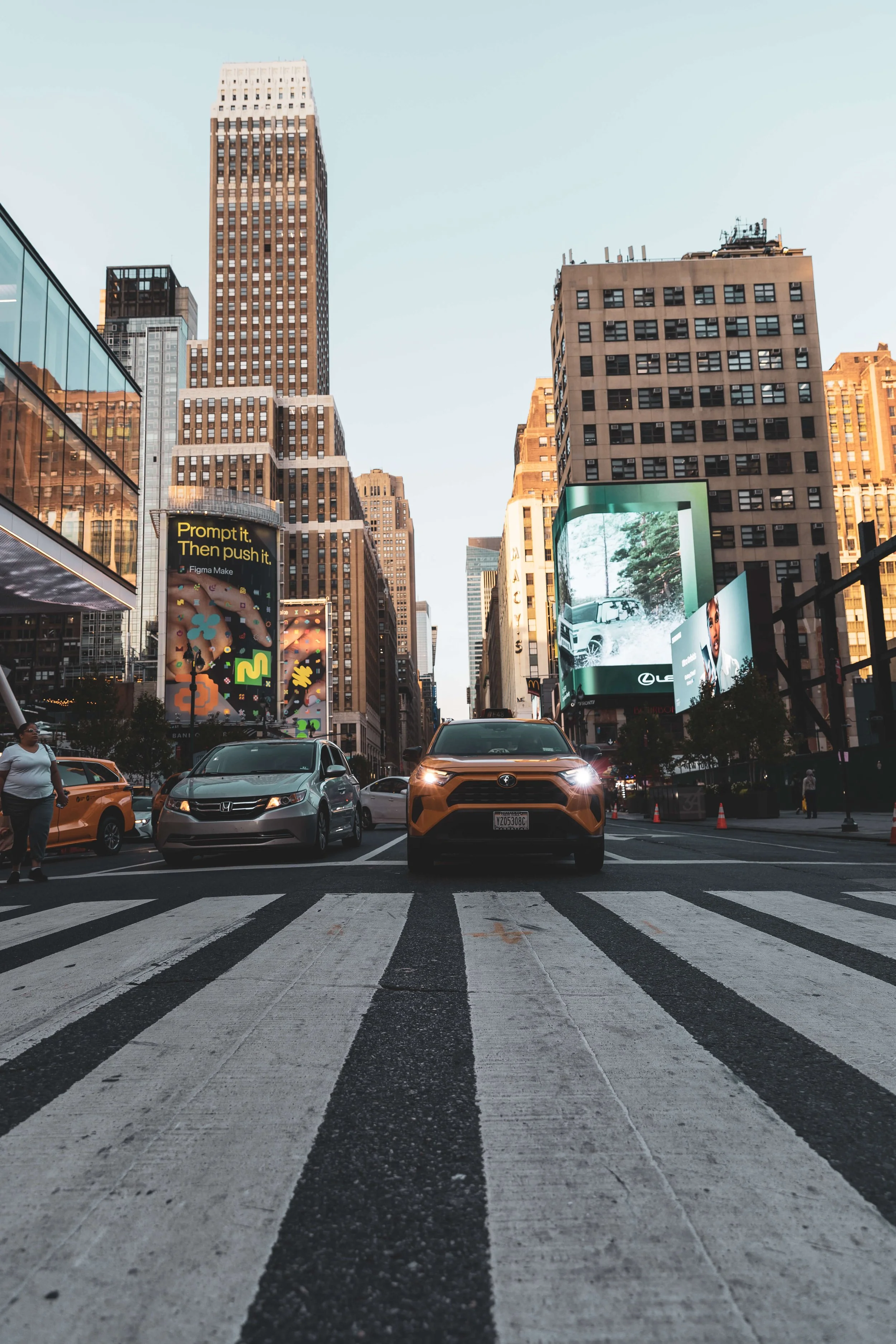 City street with crosswalk, cars, and tall buildings with digital billboards in the background.