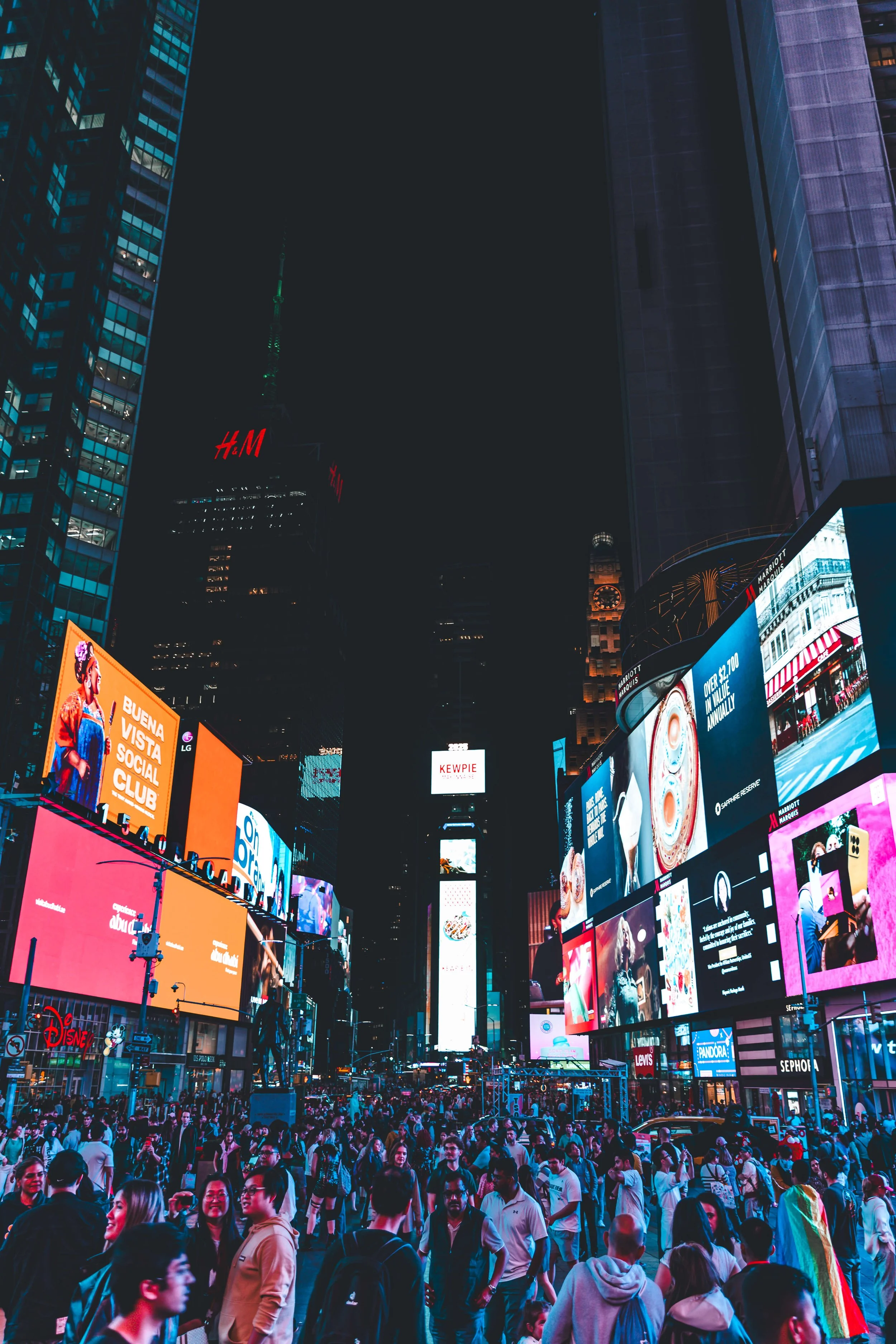 Crowded intersection in Times Square, New York City, at night with bright digital billboards and neon signs against dark skyscrapers.