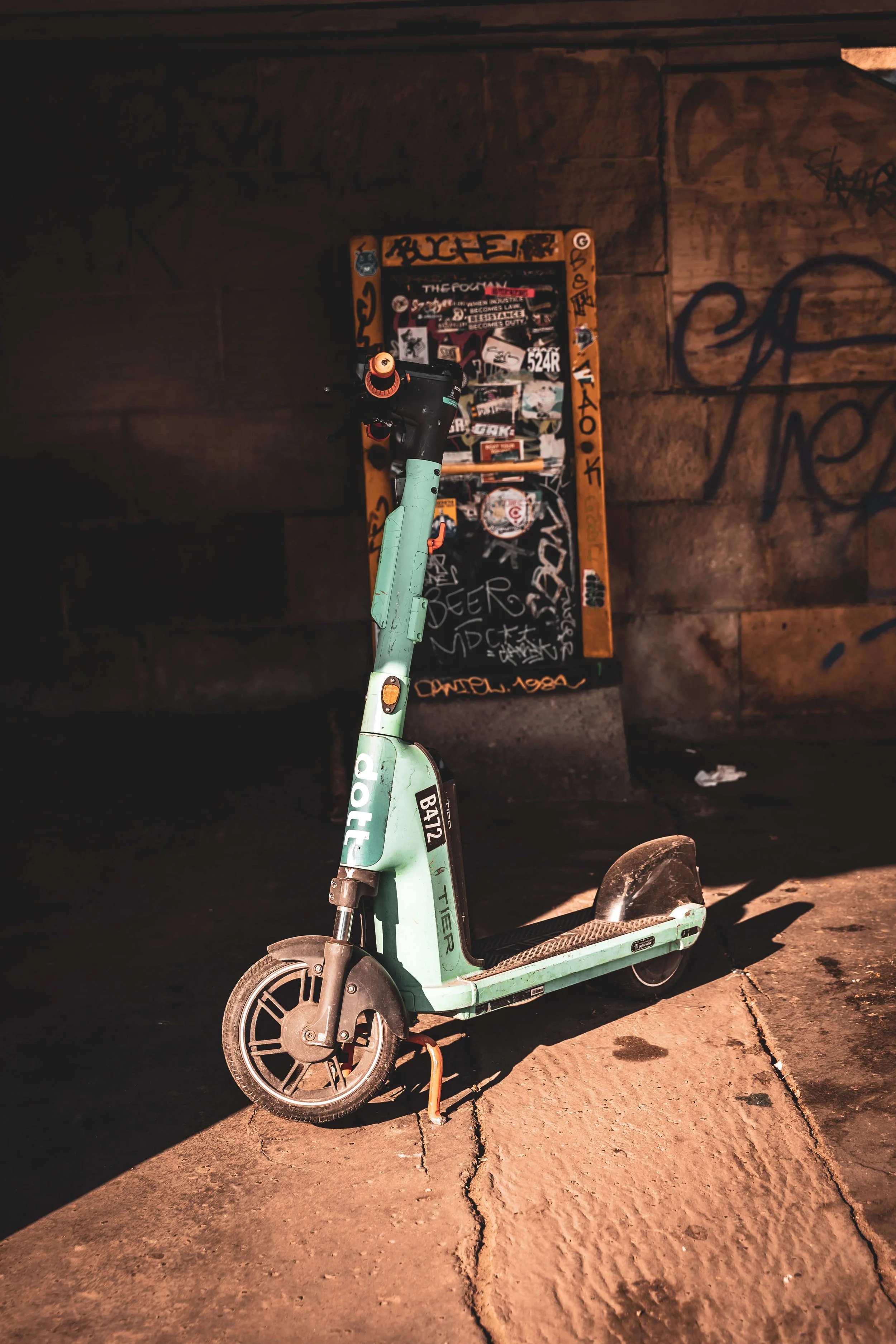 A mint green electric scooter parked on a cracked sidewalk against a graffiti-covered wall.