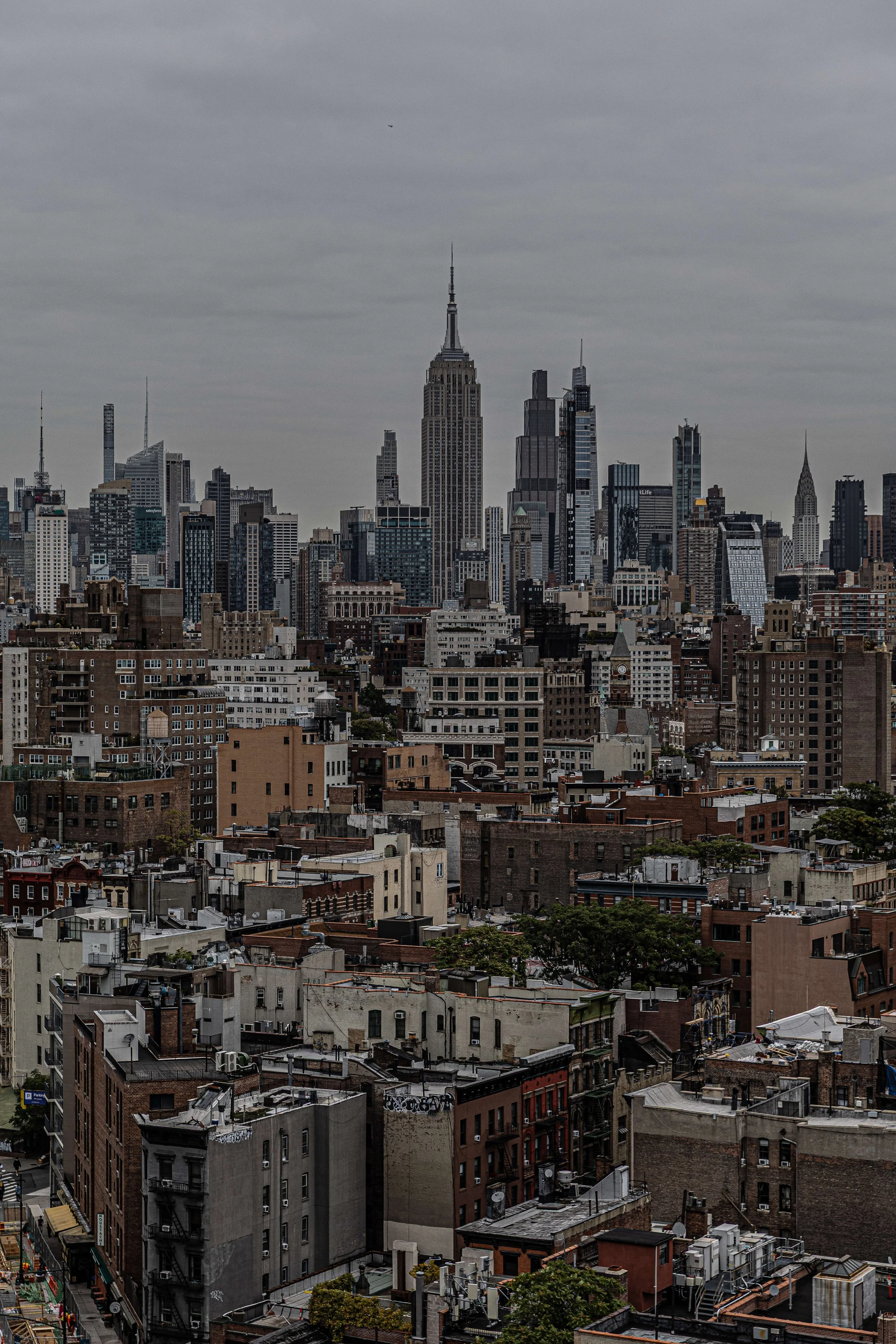 View of New York City skyline with Empire State Building and other skyscrapers under a cloudy sky.