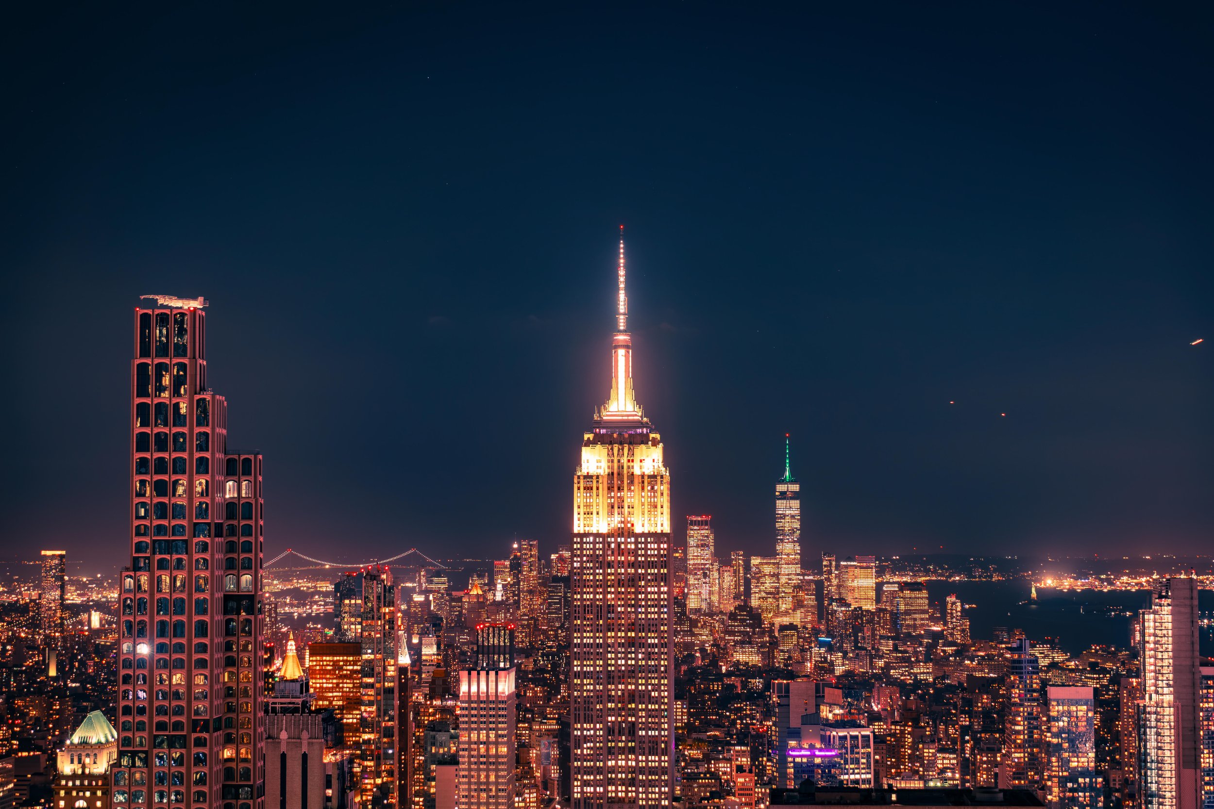 Night view of New York City skyline with illuminated Empire State Building and other skyscrapers.
