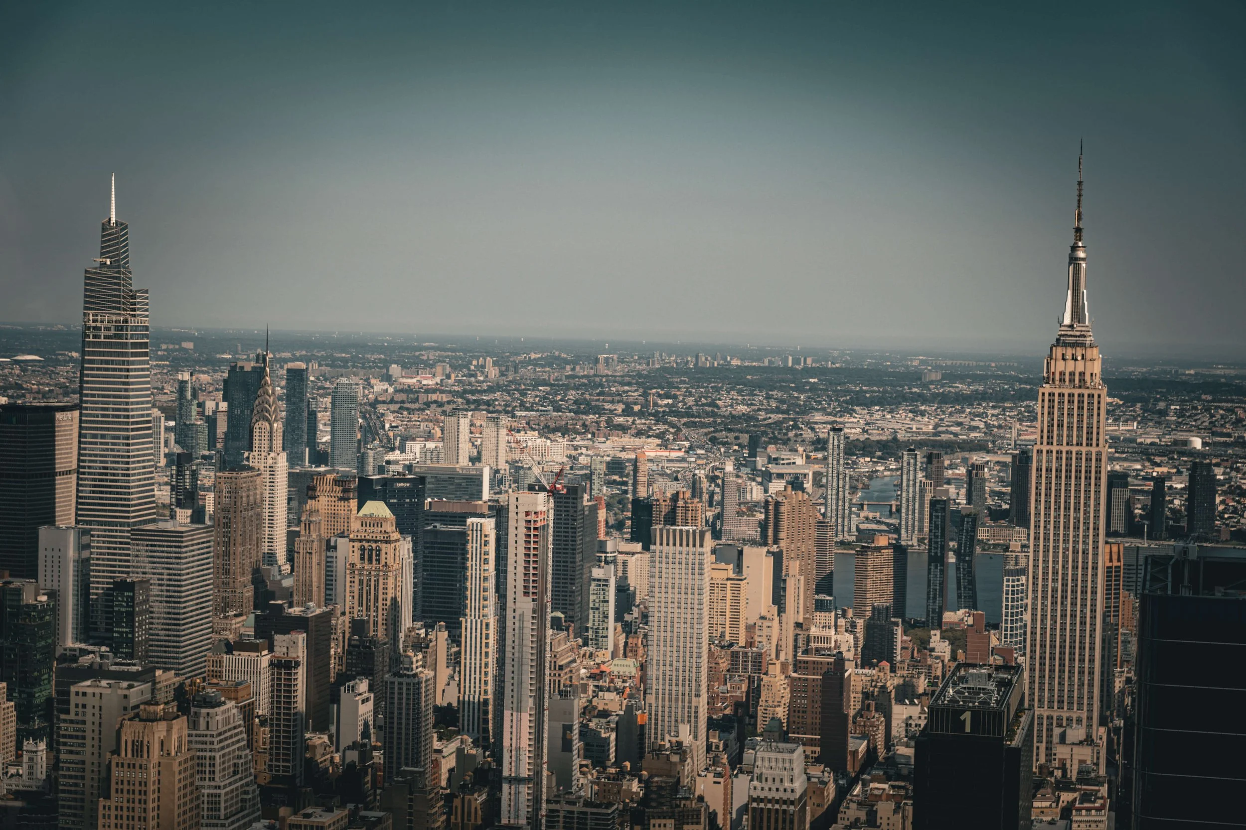 Aerial view of New York City skyline with Empire State Building and other skyscrapers under a clear sky.
