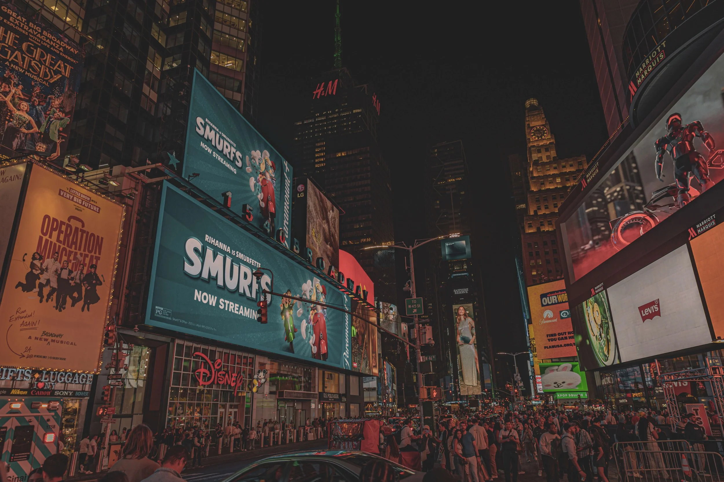 Nighttime view of Times Square in New York City filled with illuminated billboards and a crowd of people on the streets.