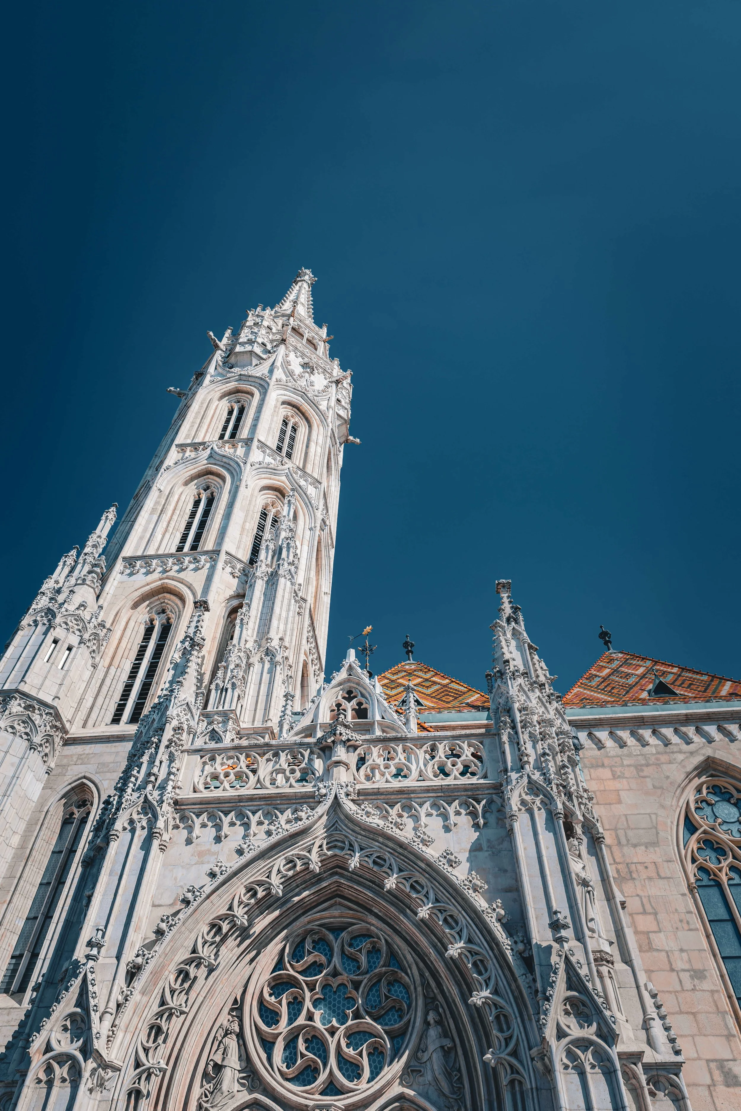 A Gothic cathedral with detailed stone carvings, tall spires, and ornate stained glass windows under a clear blue sky.