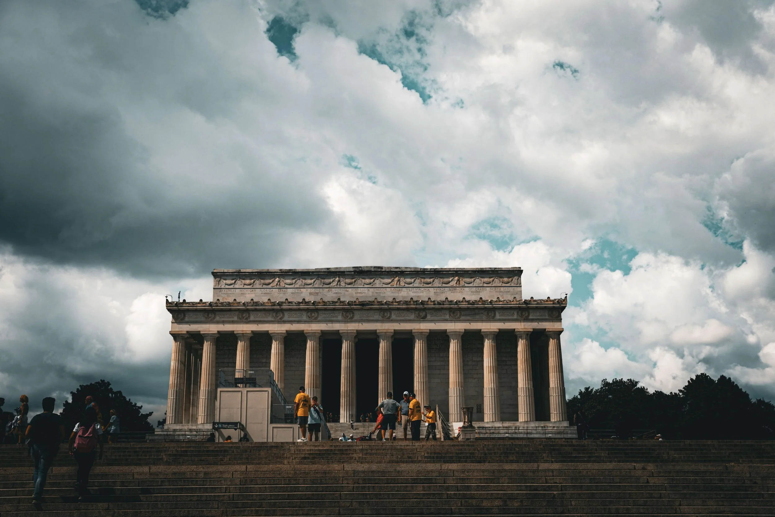 Lincoln Memorial in Washington D.C. under a cloudy sky, with people walking up the steps.