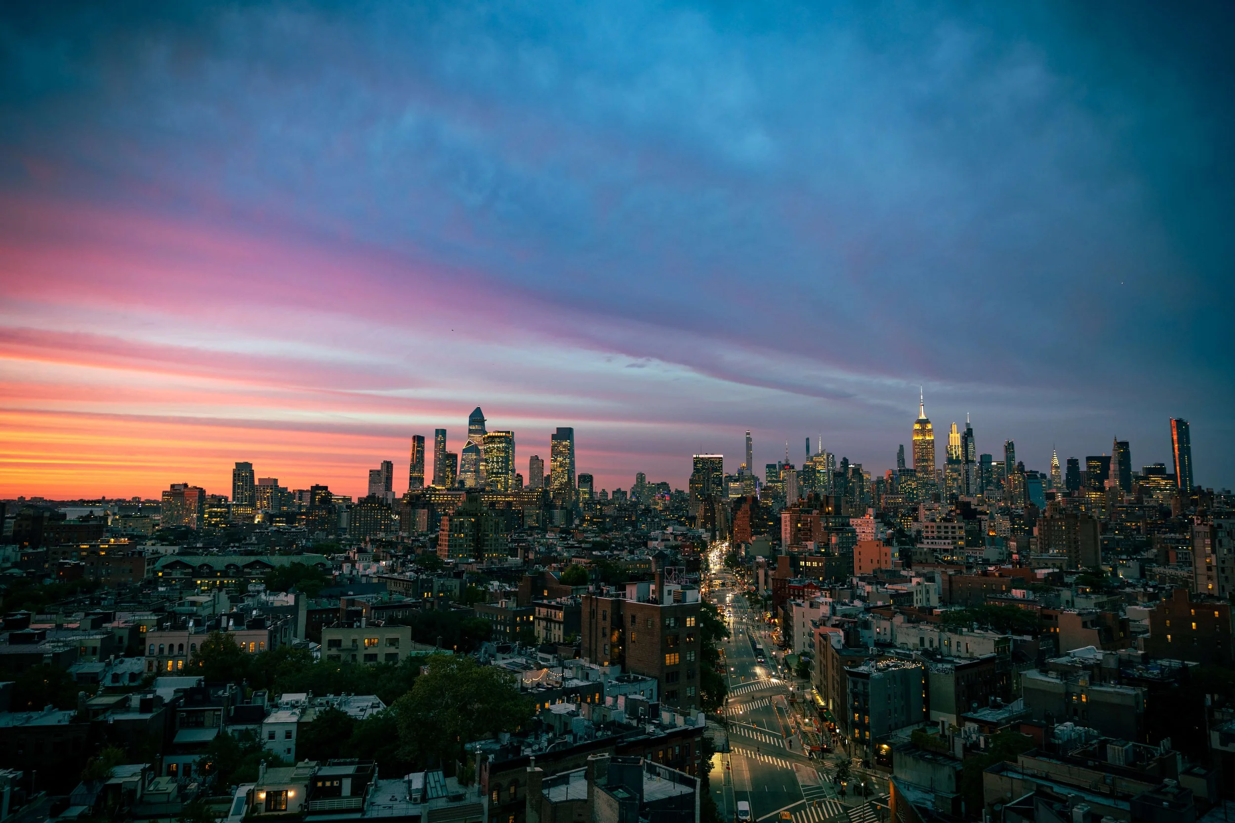 City skyline of New York City at sunset with colorful sky and illuminated buildings.