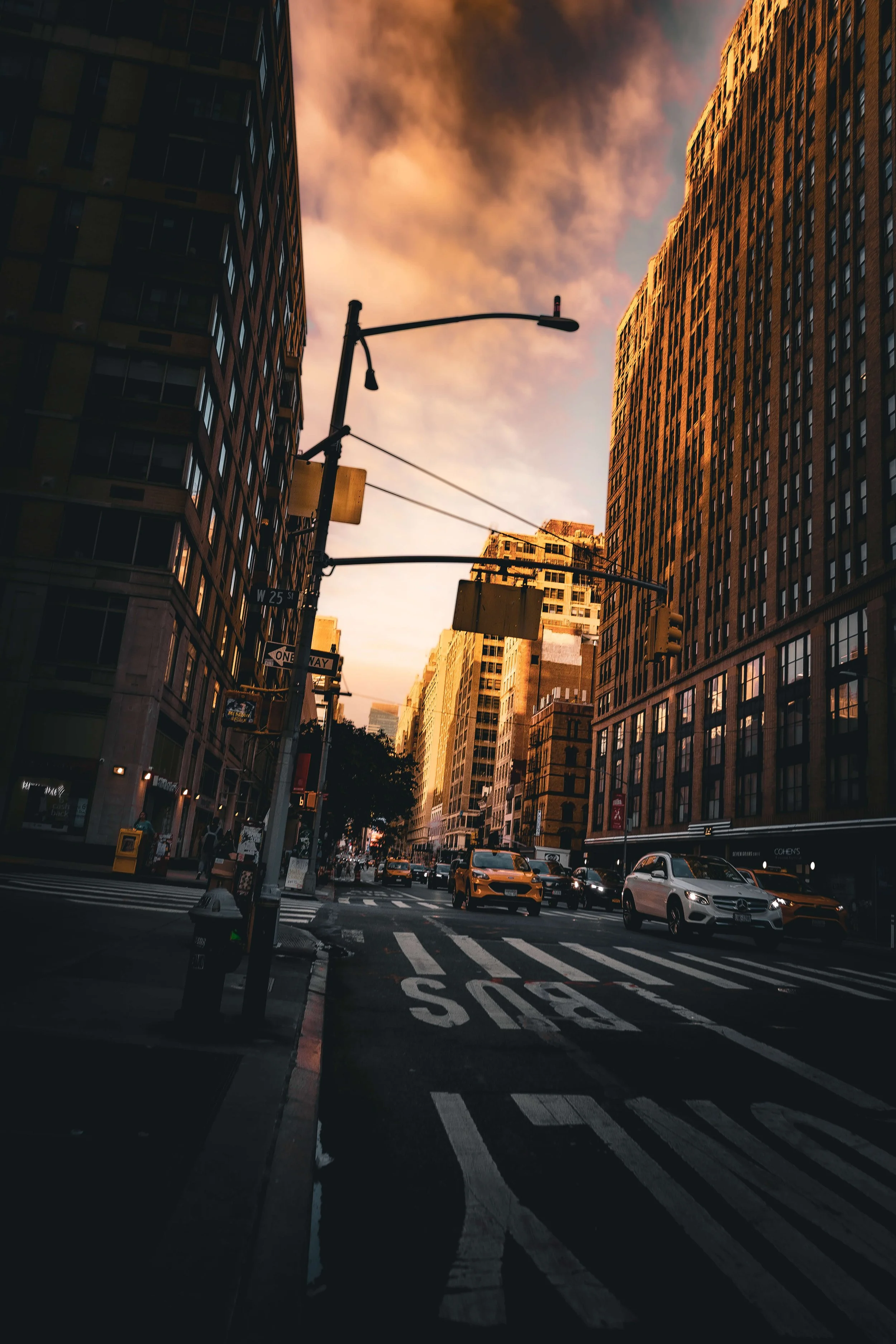 City street scene during sunset with tall buildings, cars, and traffic lights.