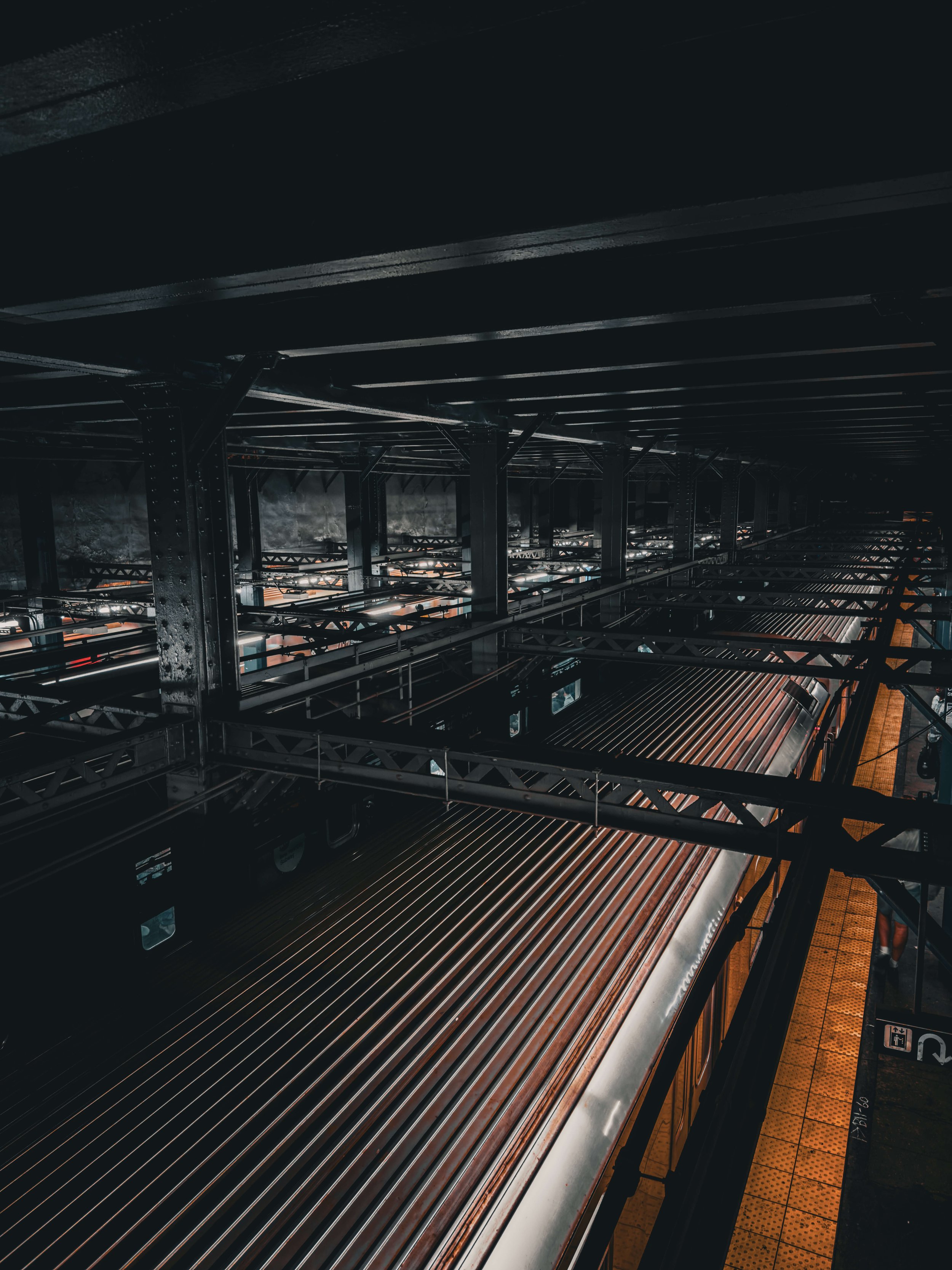 Dark underground train station with metal beams and a train on the platform.