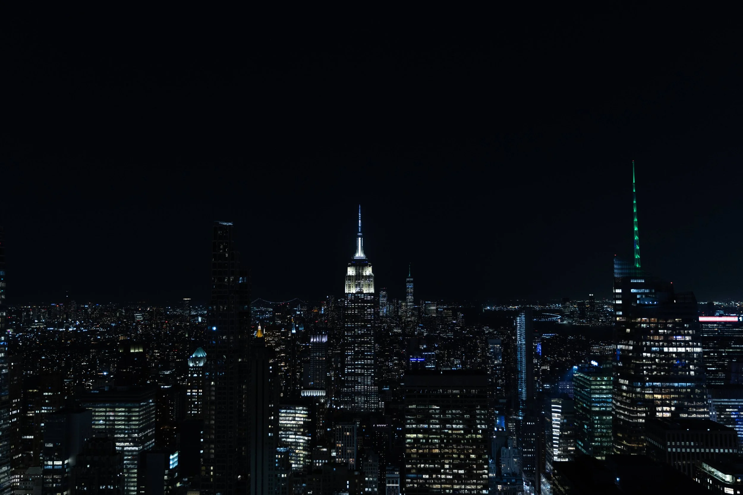 Nighttime view of New York City skyline with illuminated buildings and the Empire State Building in the center.