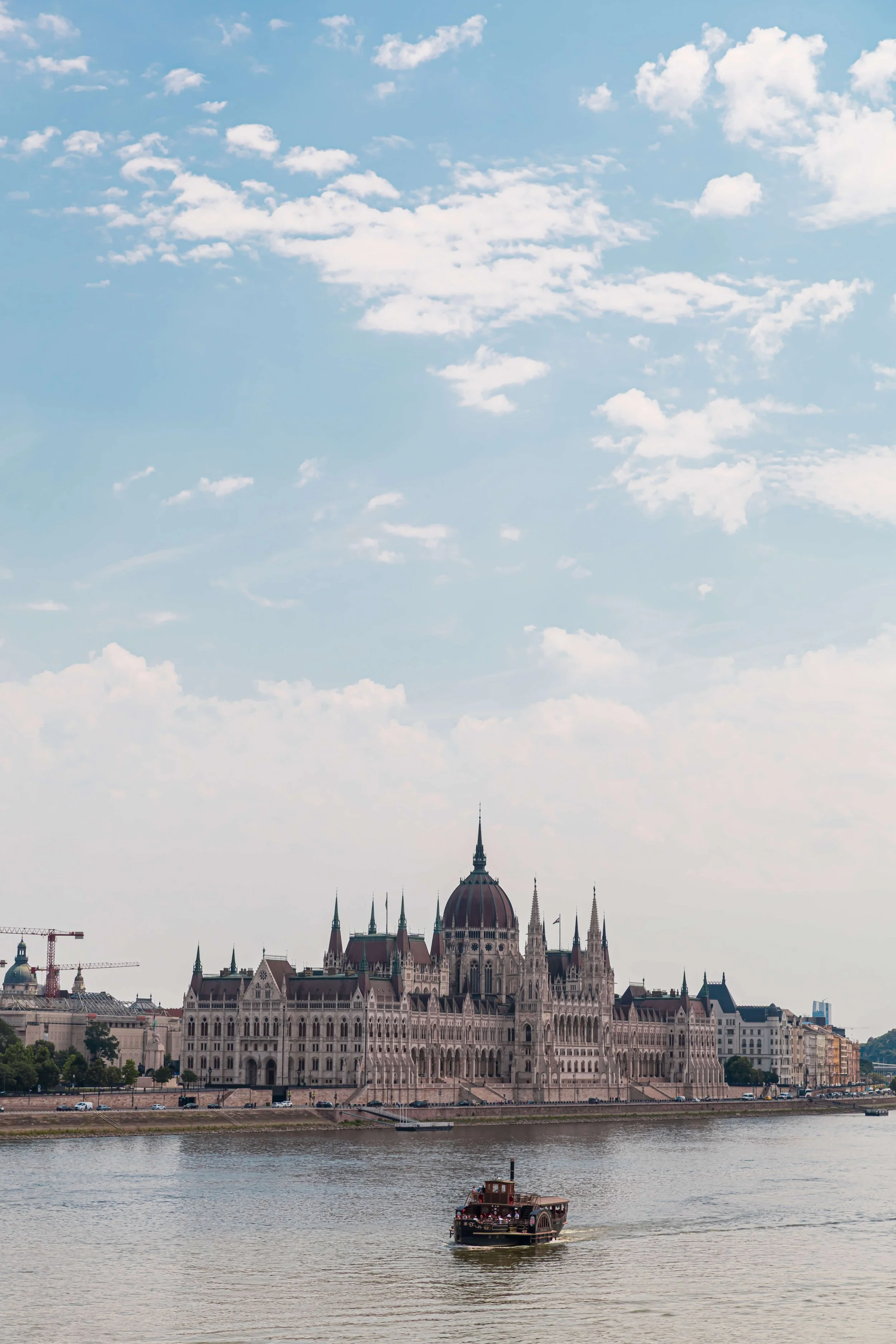 View of the Hungarian Parliament building along the Danube River with a boat in the foreground and a cloudy sky.