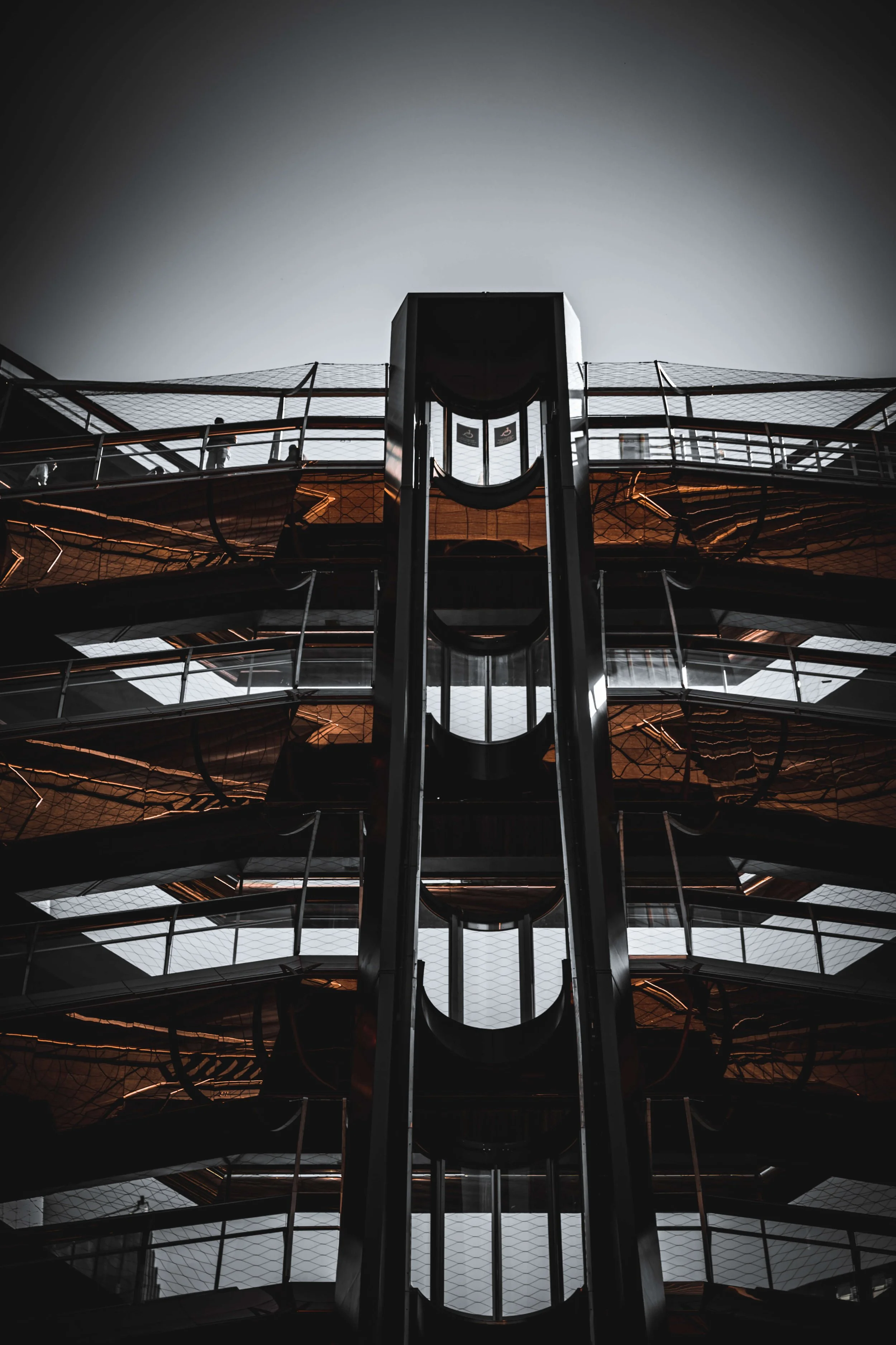 Modern, multi-story glass and metal building with angular design, viewed from below, with overcast sky in the background.