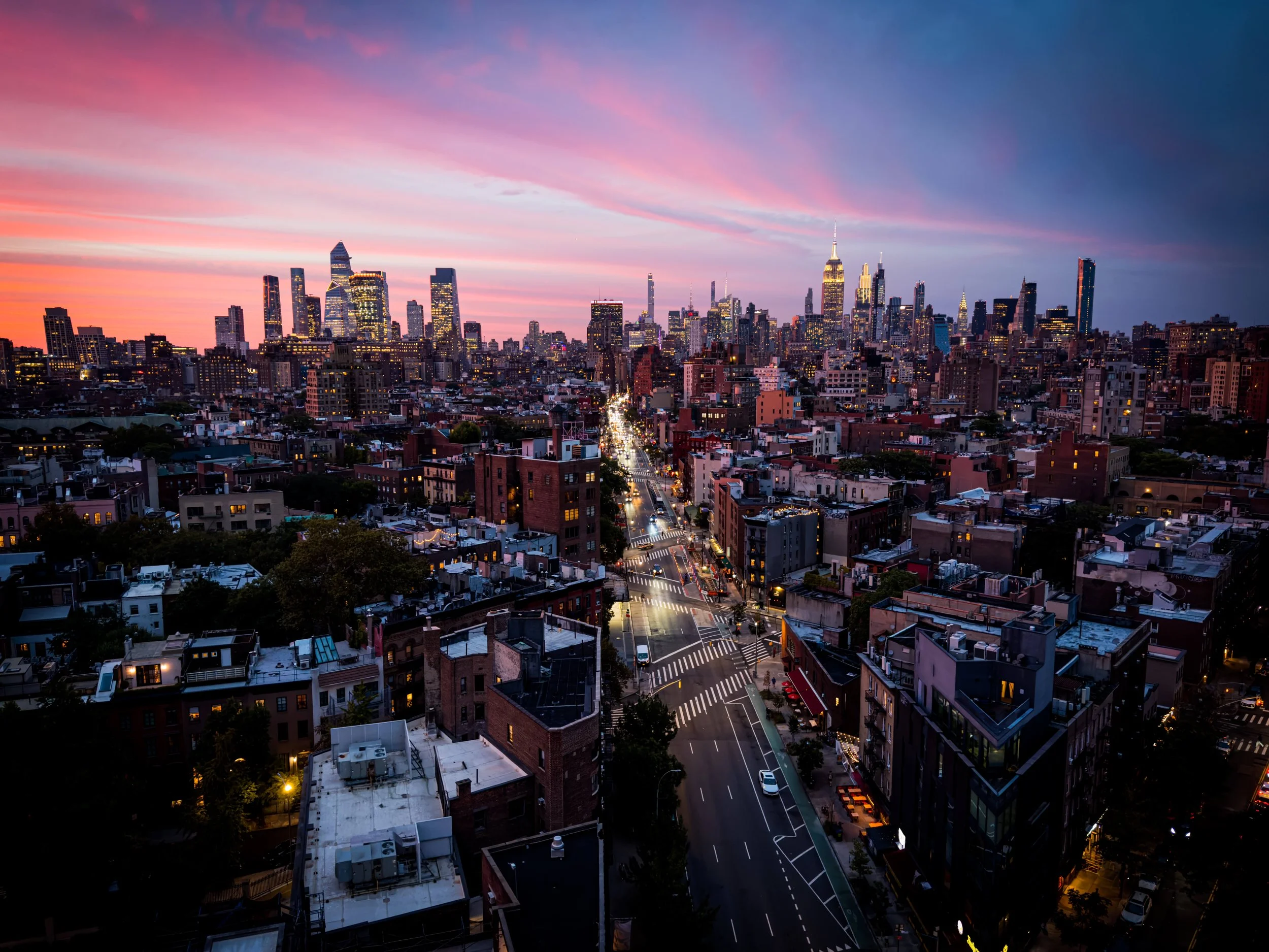 City skyline at sunset with pink and purple clouds over tall buildings and streets below.