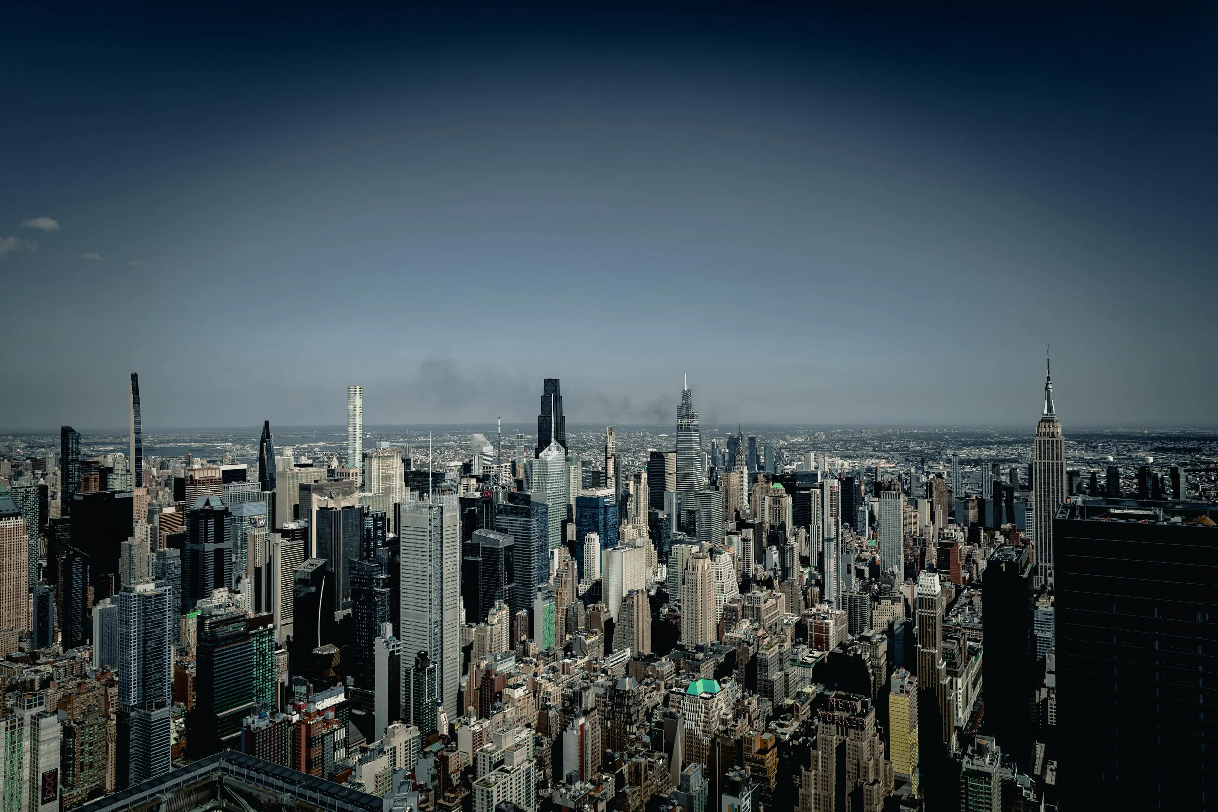 Panoramic view of New York City skyline with numerous skyscrapers including Empire State Building, during daytime with clear sky.