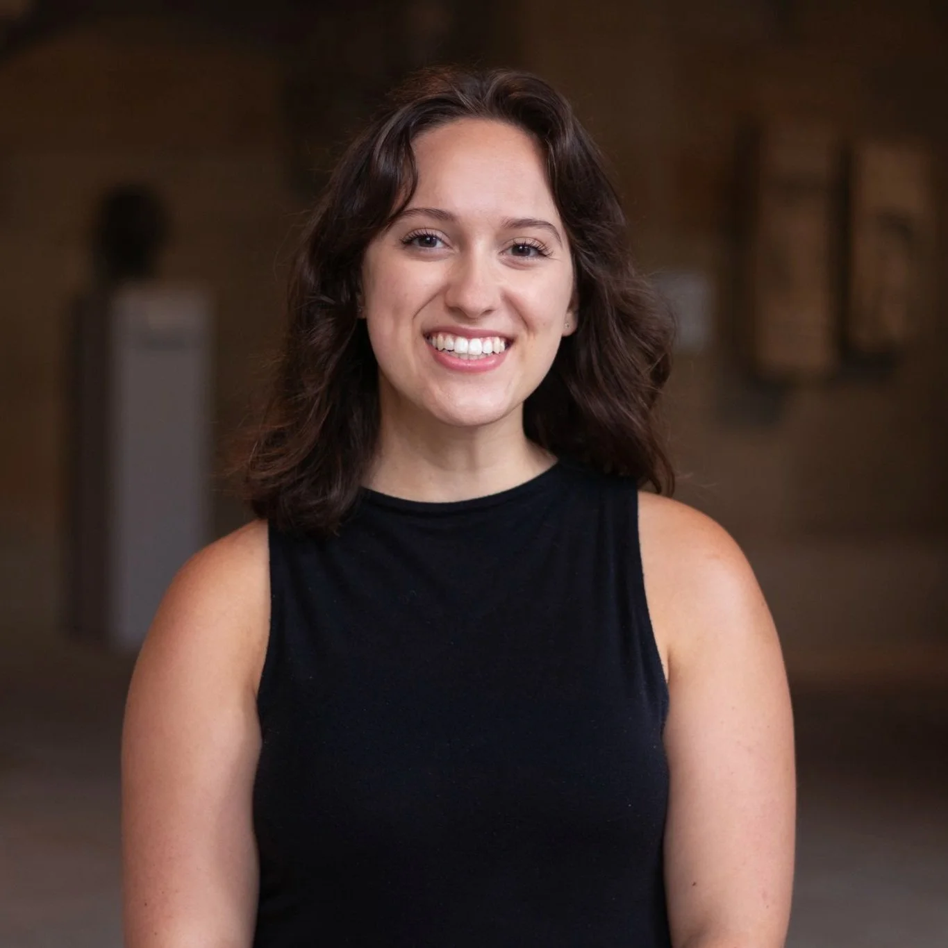 Carlin Steere, a white woman with shoulder-length brown hair and a black sleeveless top, smiles.