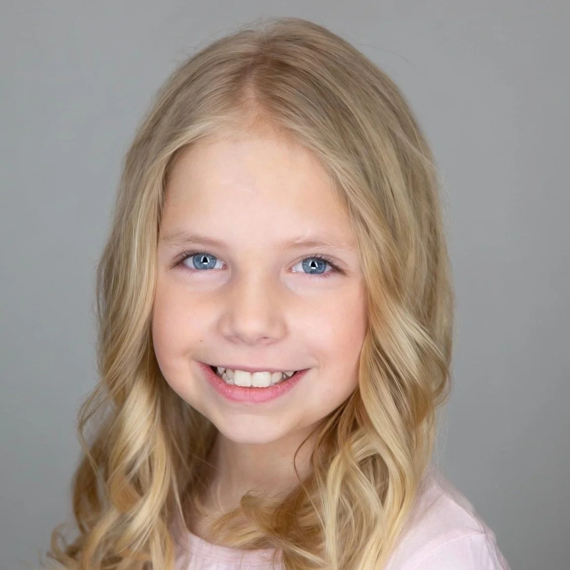 Child with long blonde hair smiles at camera