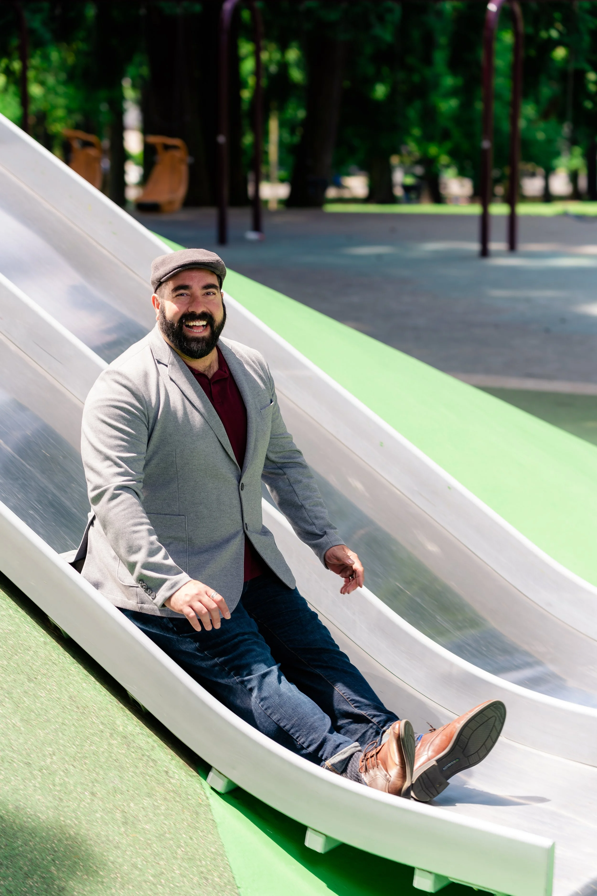 Michael Eric Jonas sliding down a slide on a play structure on a sunny day.