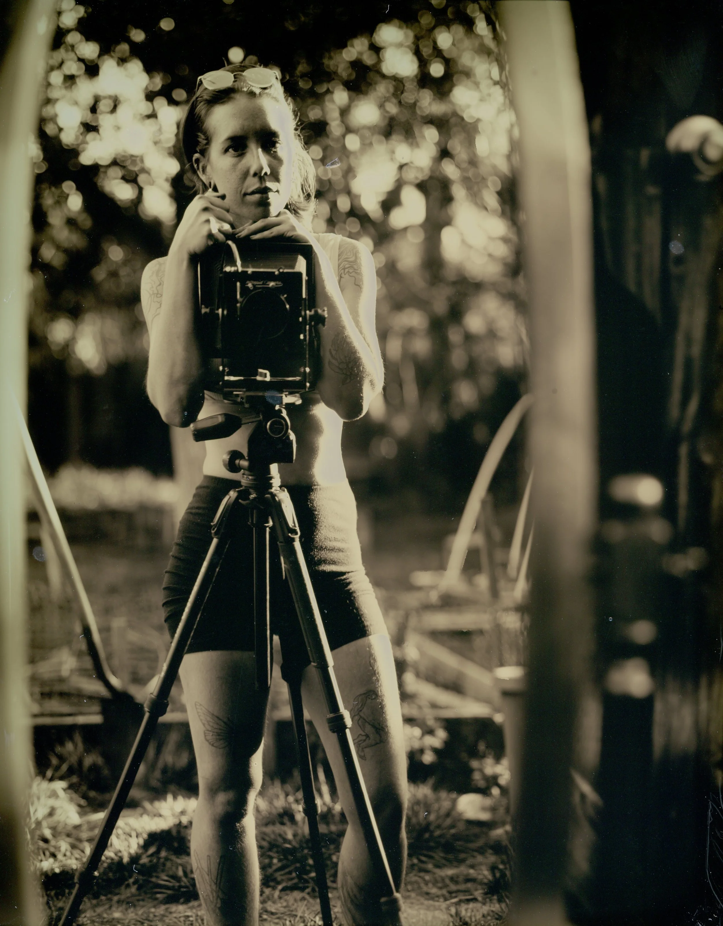 Vintage sepia-toned photo of a person holding a large camera on a tripod outdoors.
