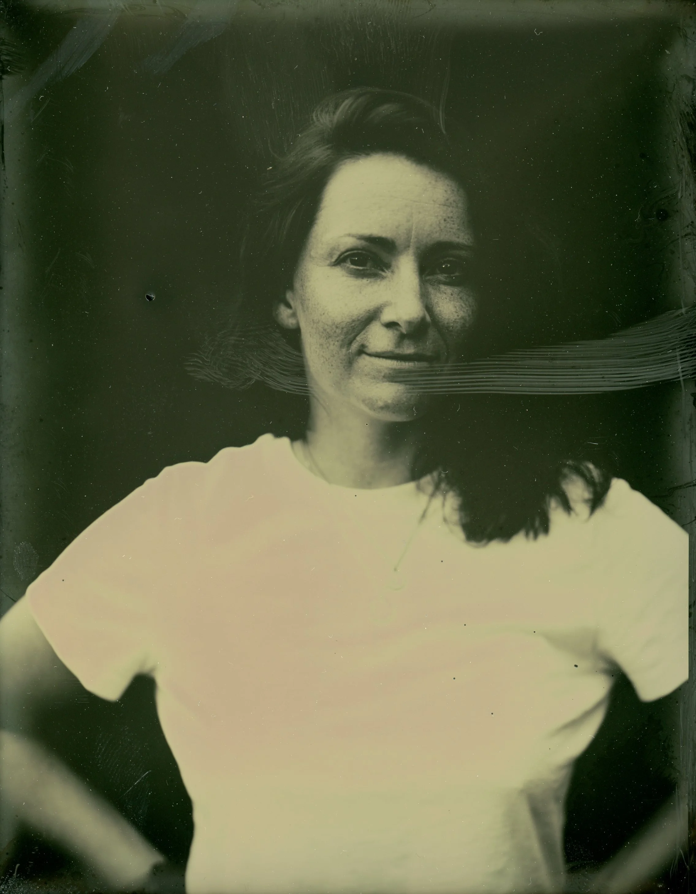 Vintage-style portrait of a person in a white shirt, looking directly at the camera with a neutral expression, against a dark background.