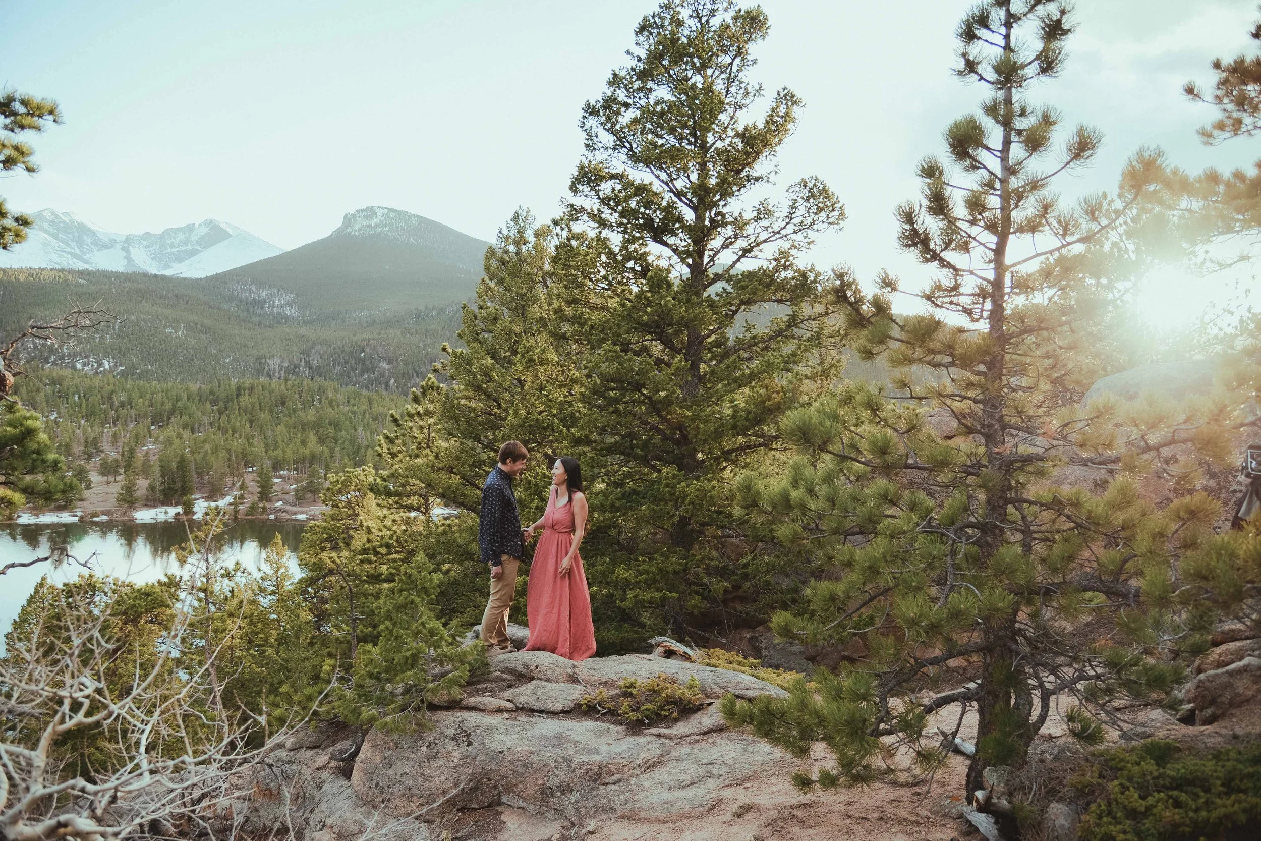 A couple in nature surrounded by pine trees and distant mountains.