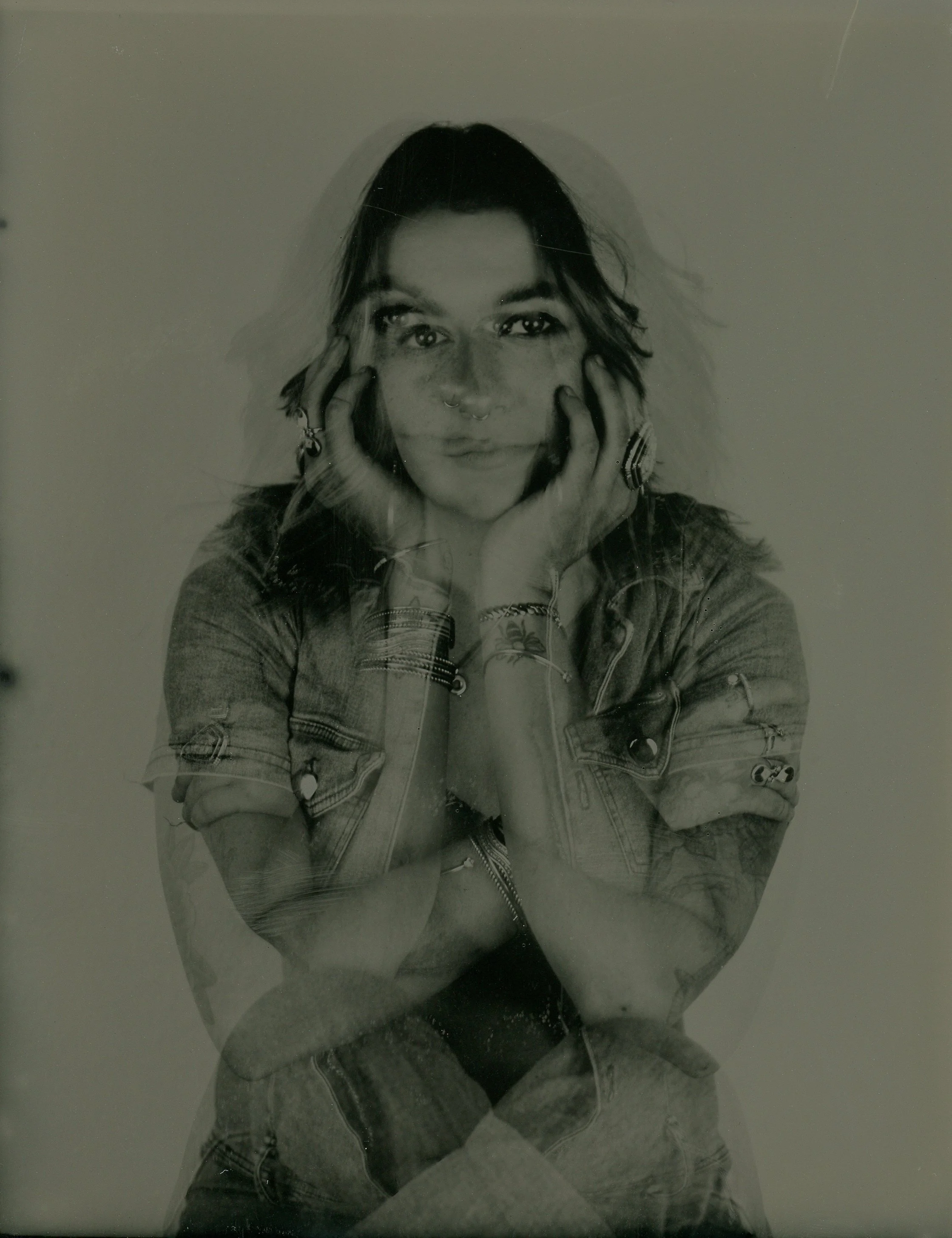 Double exposure image of a person seated with hands resting on their face, wearing denim and jewelry, creating a layered visual effect.