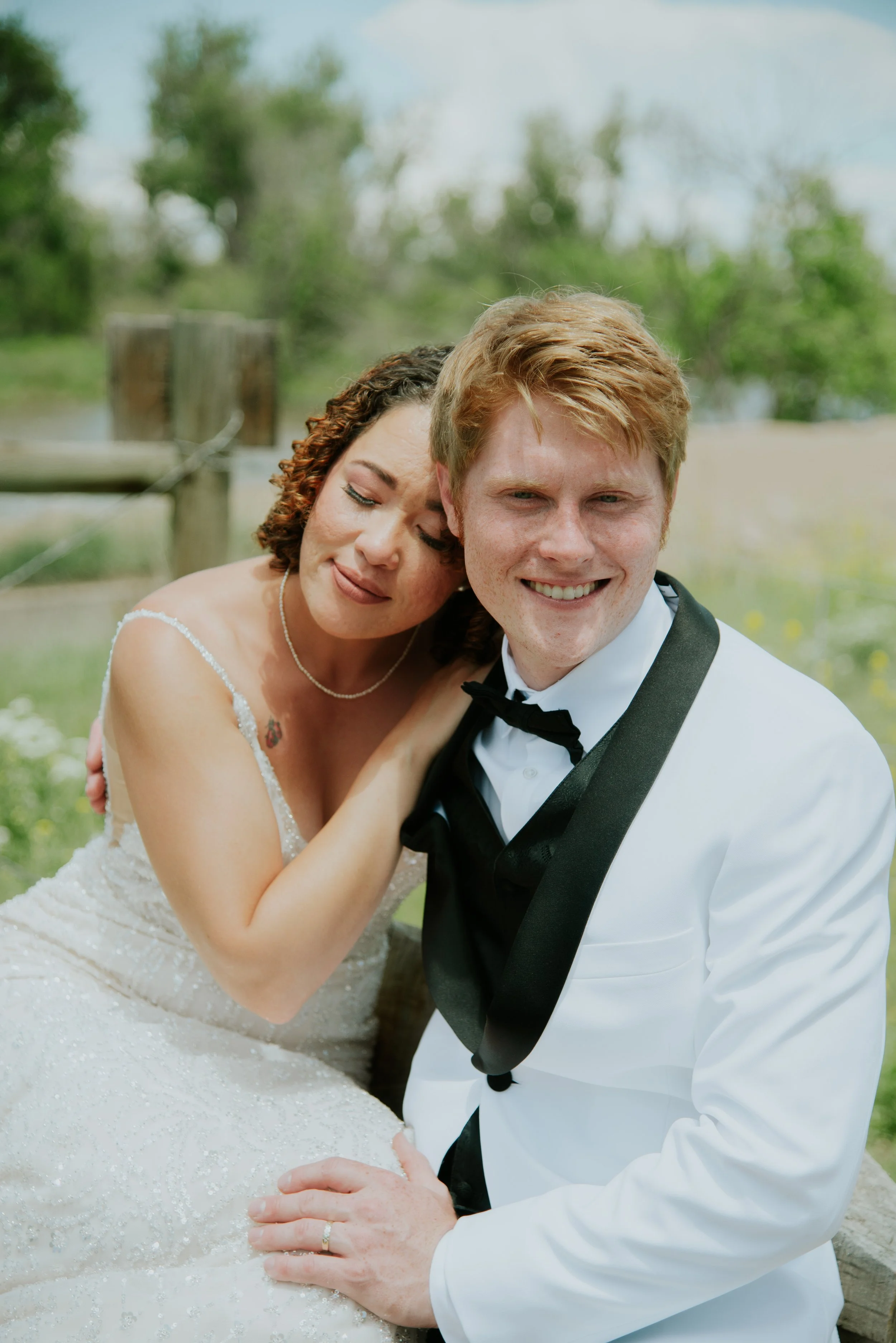 Bride and groom in formal attire smiling and sitting outdoors.