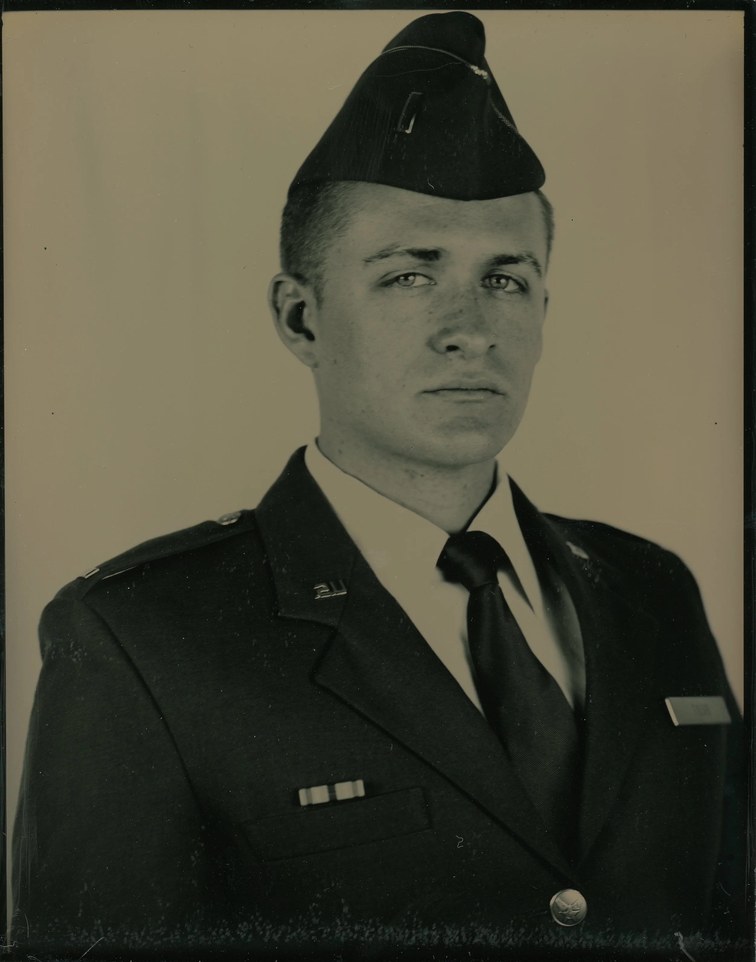 Black and white photograph of a person in military uniform with a cap, looking directly at the camera.