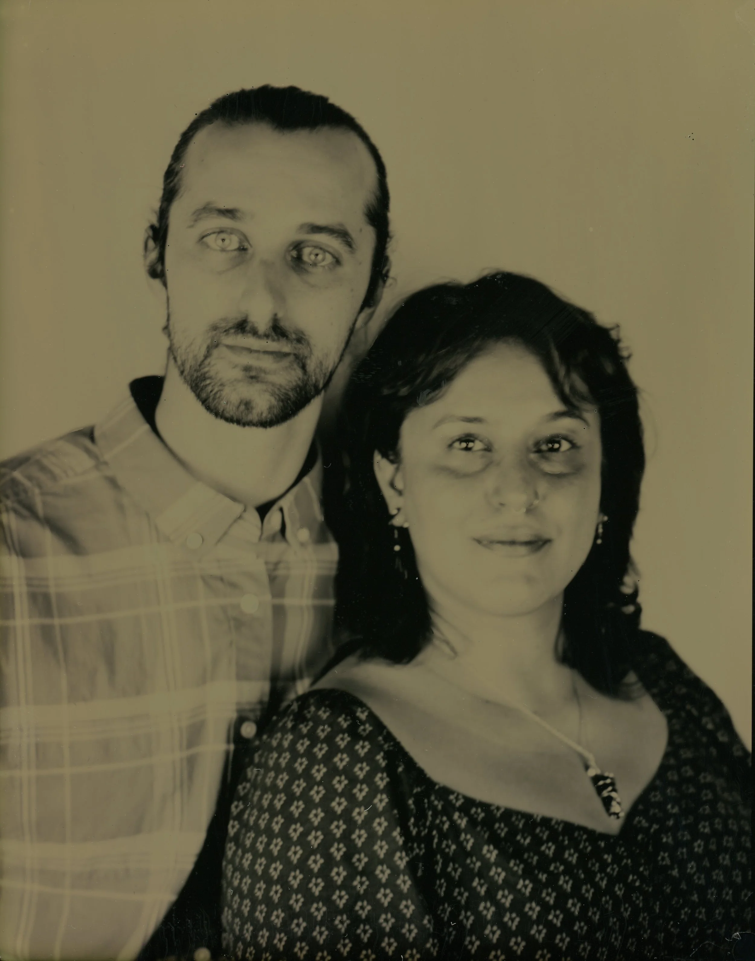 Vintage portrait of a couple; man with a beard and plaid shirt, woman with dark hair and patterned dress.