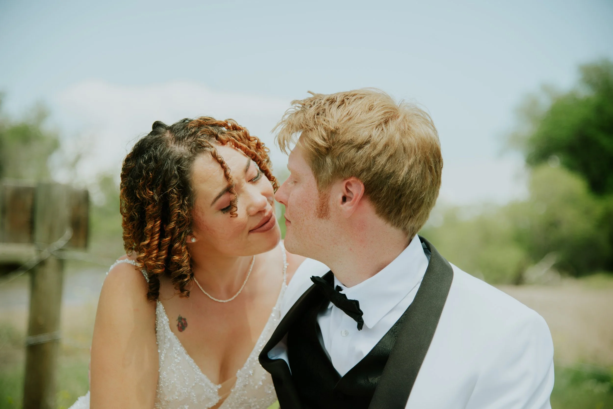 Bride and groom about to kiss outdoors, wearing wedding attire.